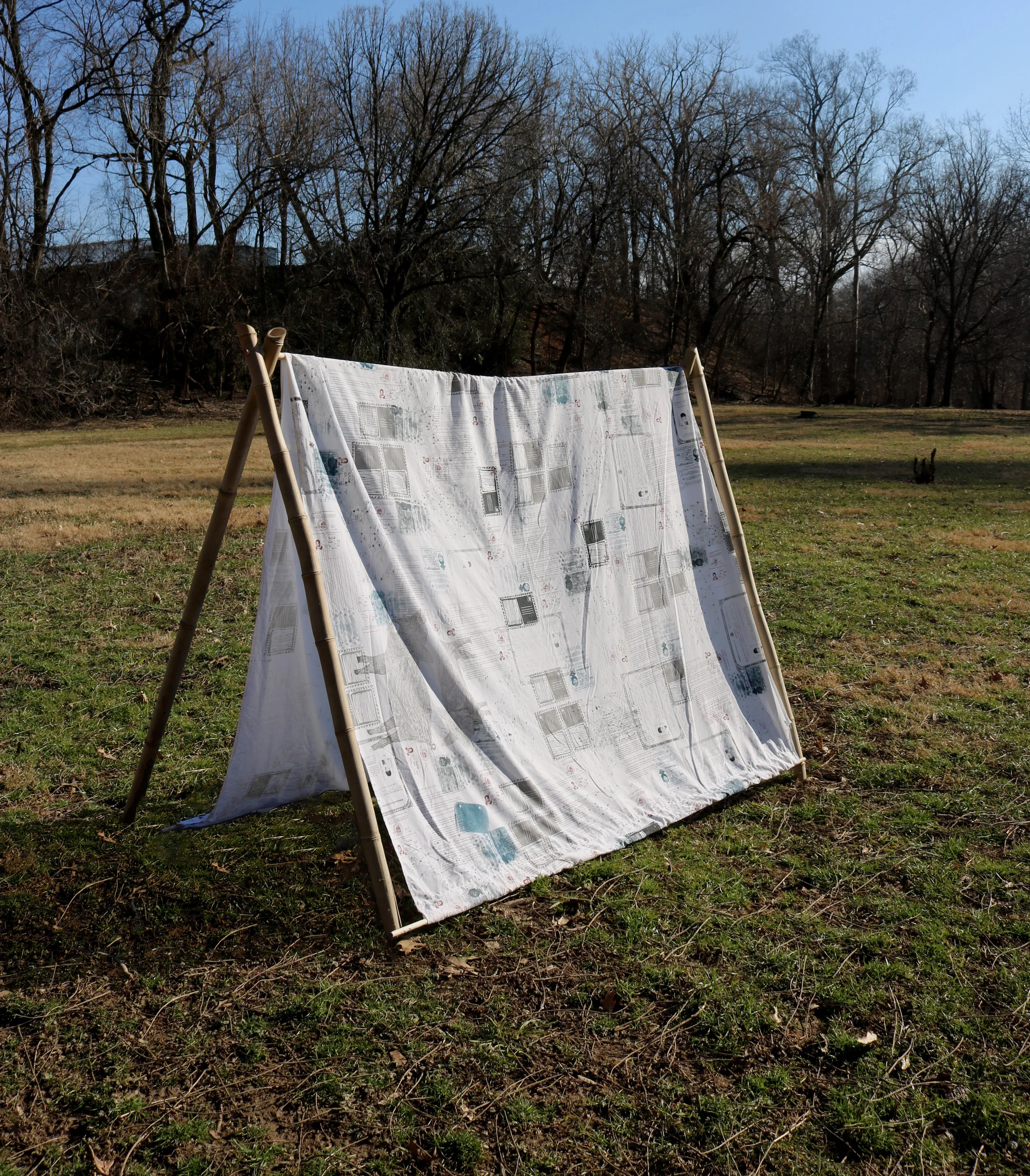 To Build a Shelter , 32” x 72” x 58,”2019 Silkscreened official government images + documents on repurposed bedsheet, a-frame tent handcrafted from foraged & dried bamboo poles.