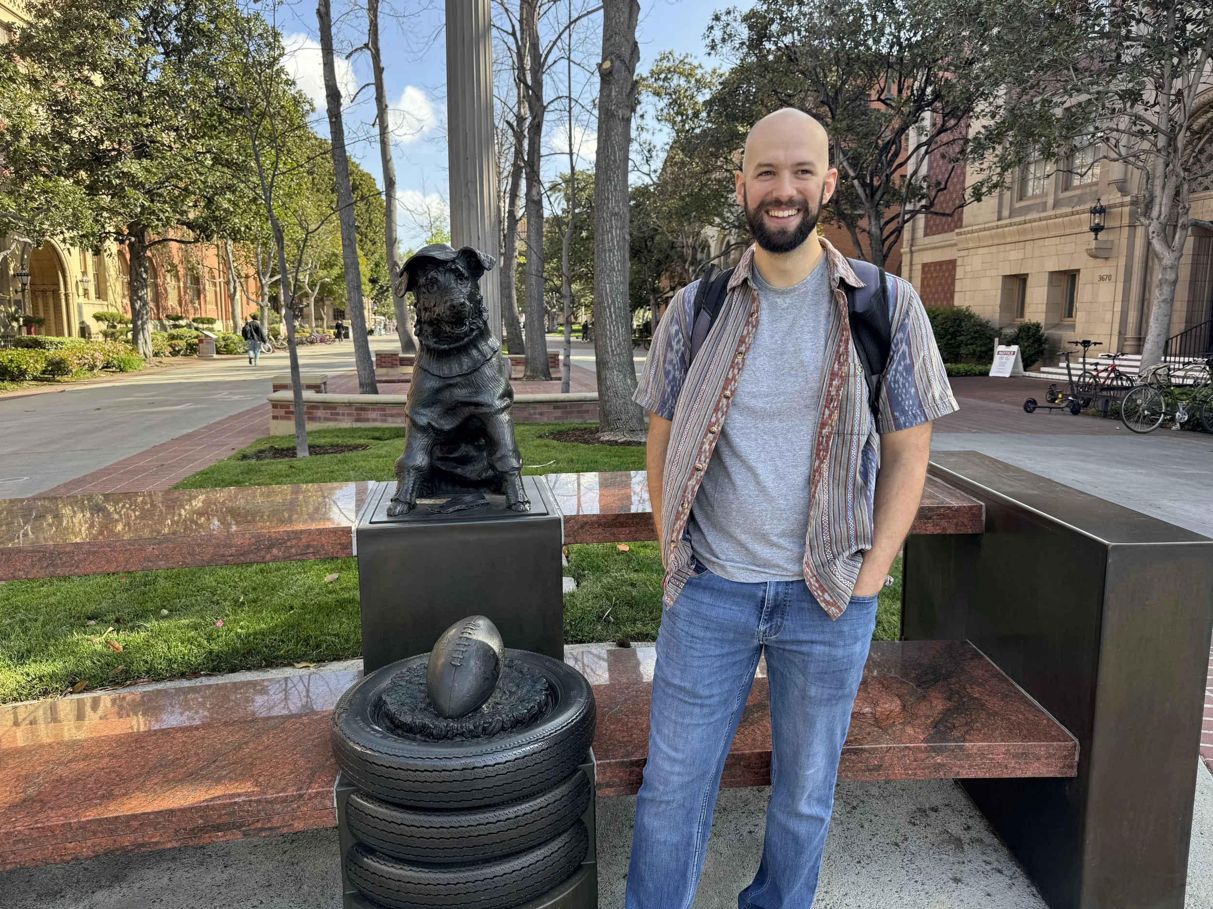 Jordan Myers, the author, smiling in front of a statue of a dog and a football