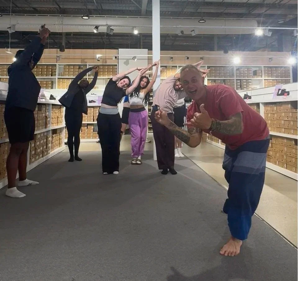 Yoga teacher smiling with students behind him doing half moon pose