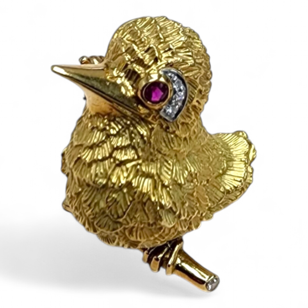 A gold brooch in the shape of a bird, with a ruby eye and diamond accents.