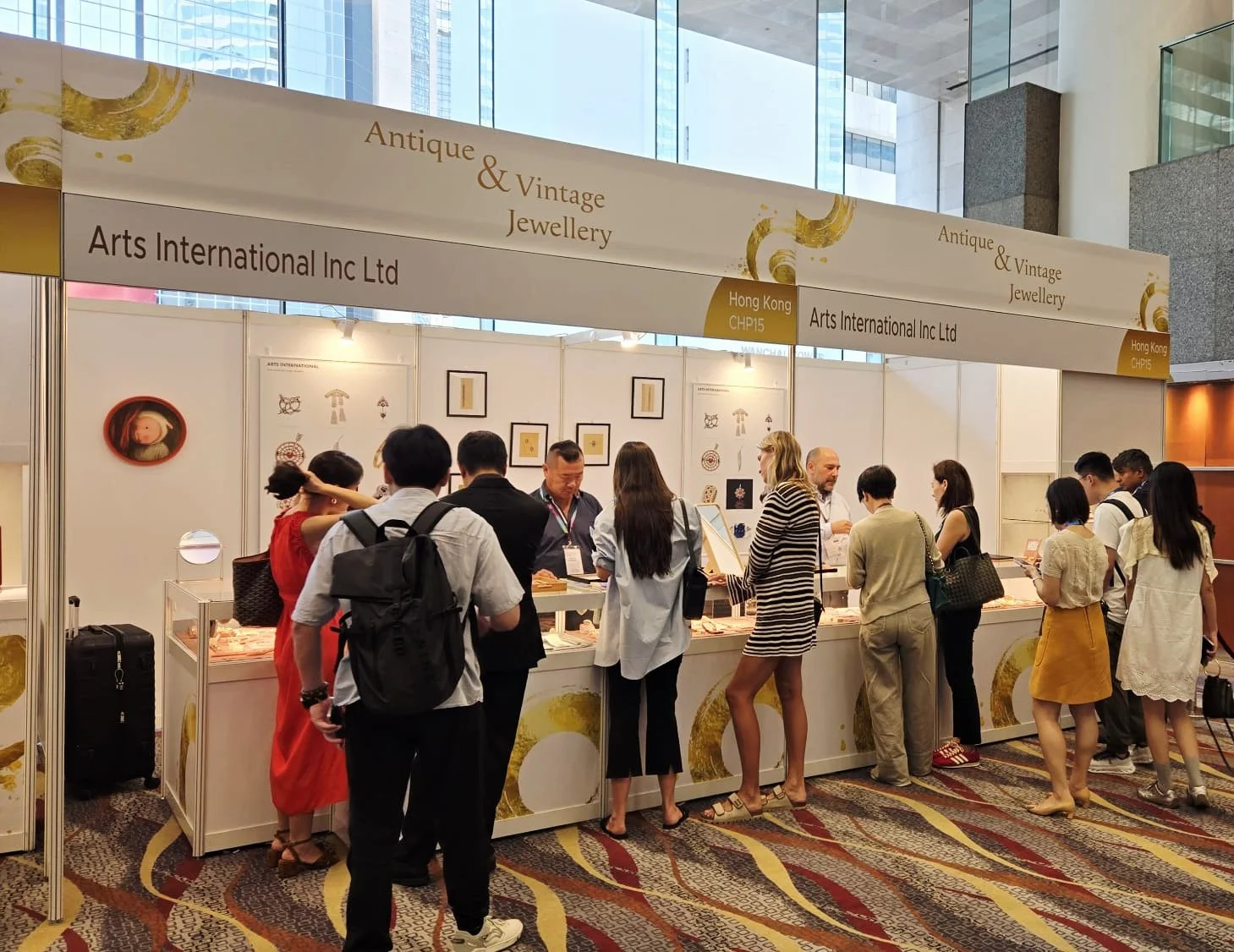 People browsing and purchasing antique and vintage jewelry at a trade show booth in a large, well-lit convention center.