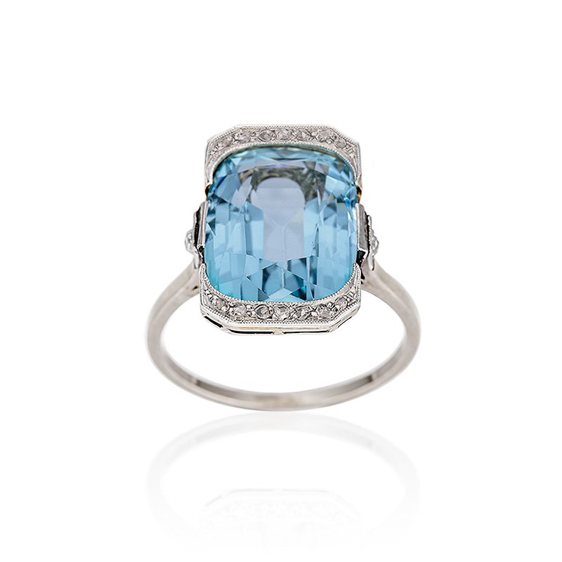 AN ART DECO AQUAMARINE AND DIAMOND RING 
The rectangular cushion cut aquamarine weighing 8.0cts, with rose cut diamond detail to each end and two shoulder diamonds, estimated total diamond weight 0.20cts,