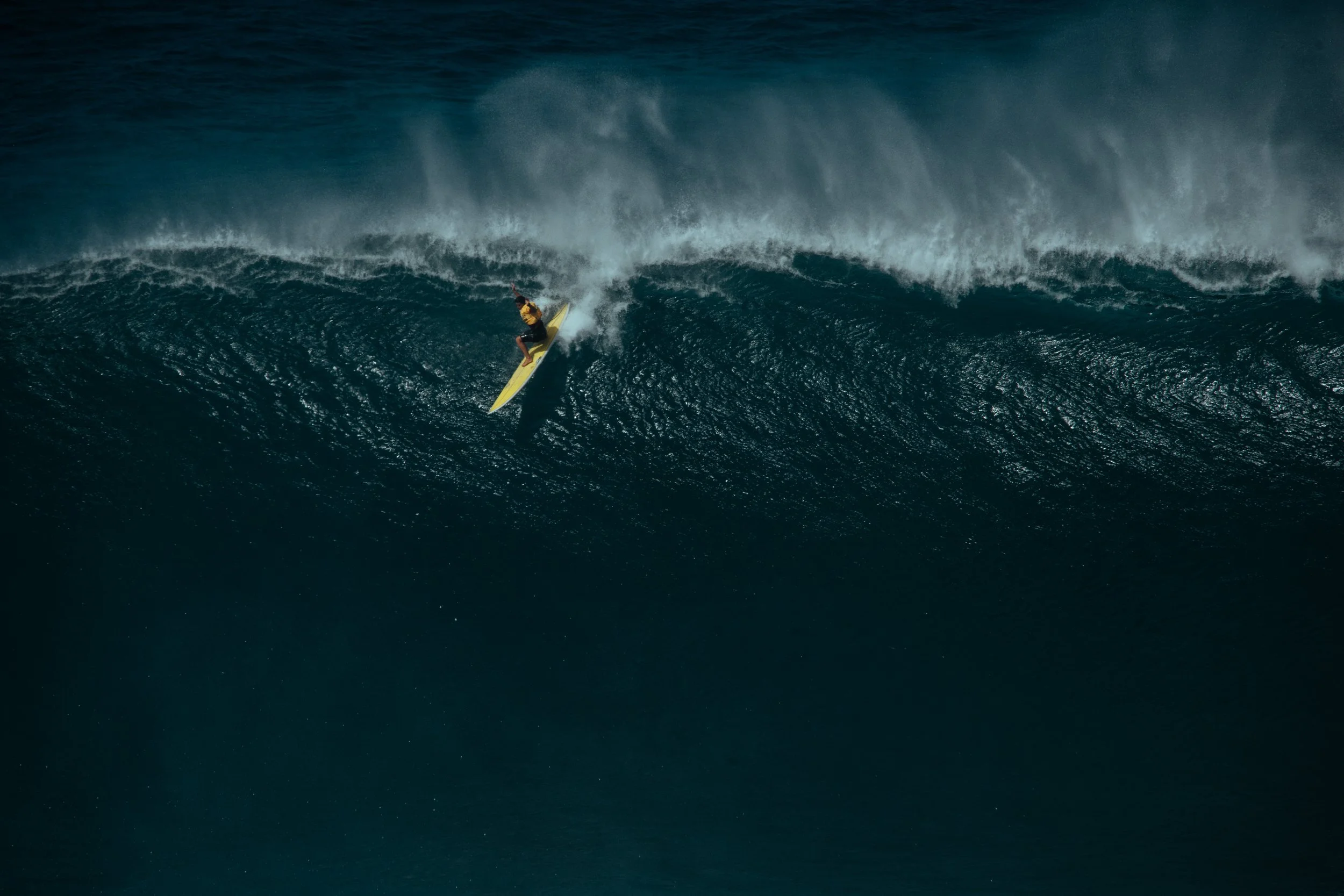 A person surfing on a large ocean wave with spray and white foam.