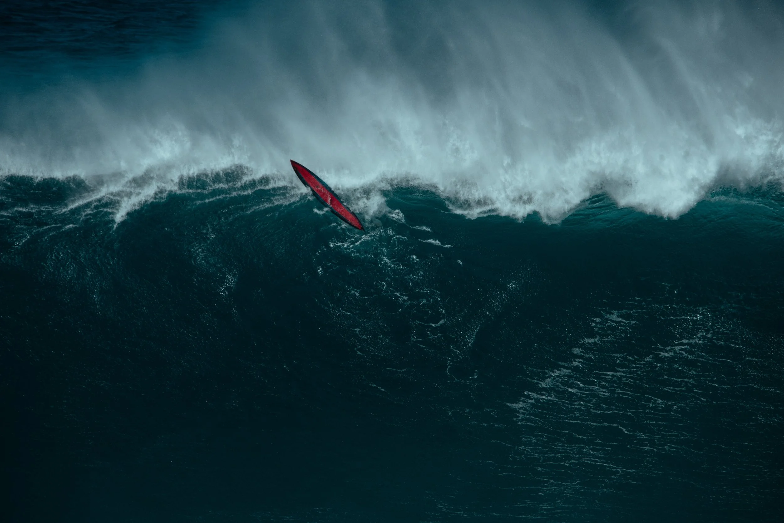A person on a red surfboard riding a large wave in the ocean.