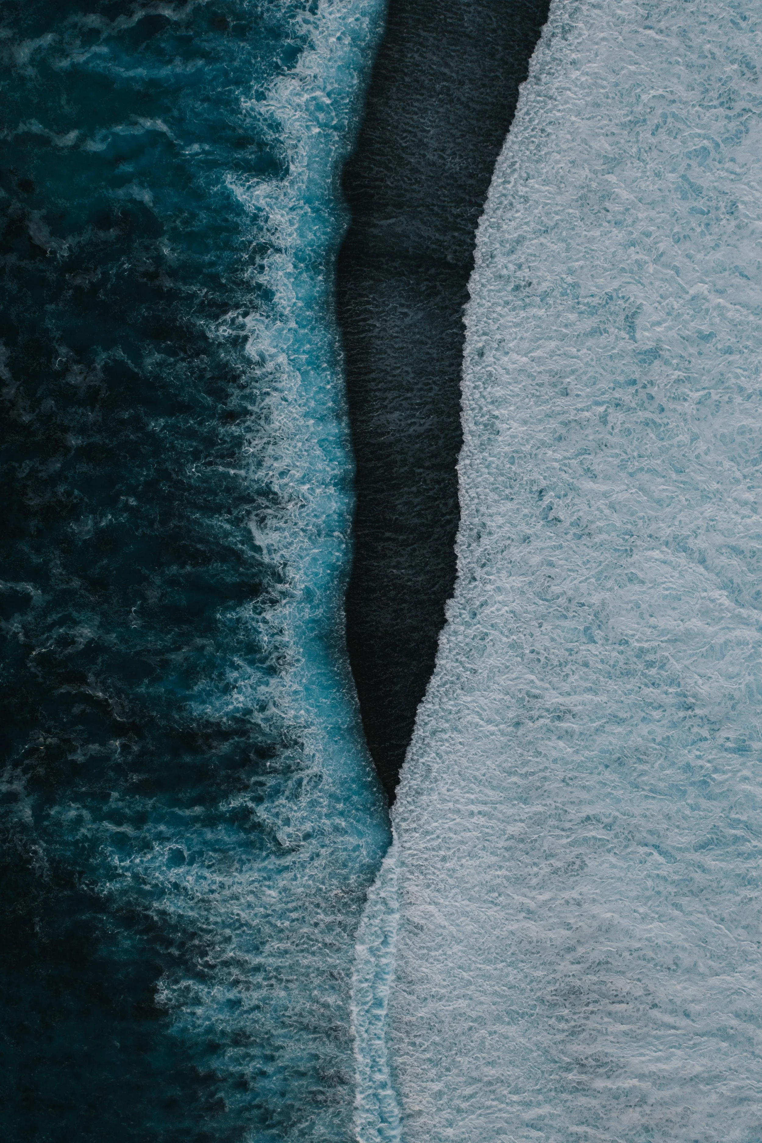 Aerial view of a large ocean wave crashing into a dark rock formation in the water, creating white foam.