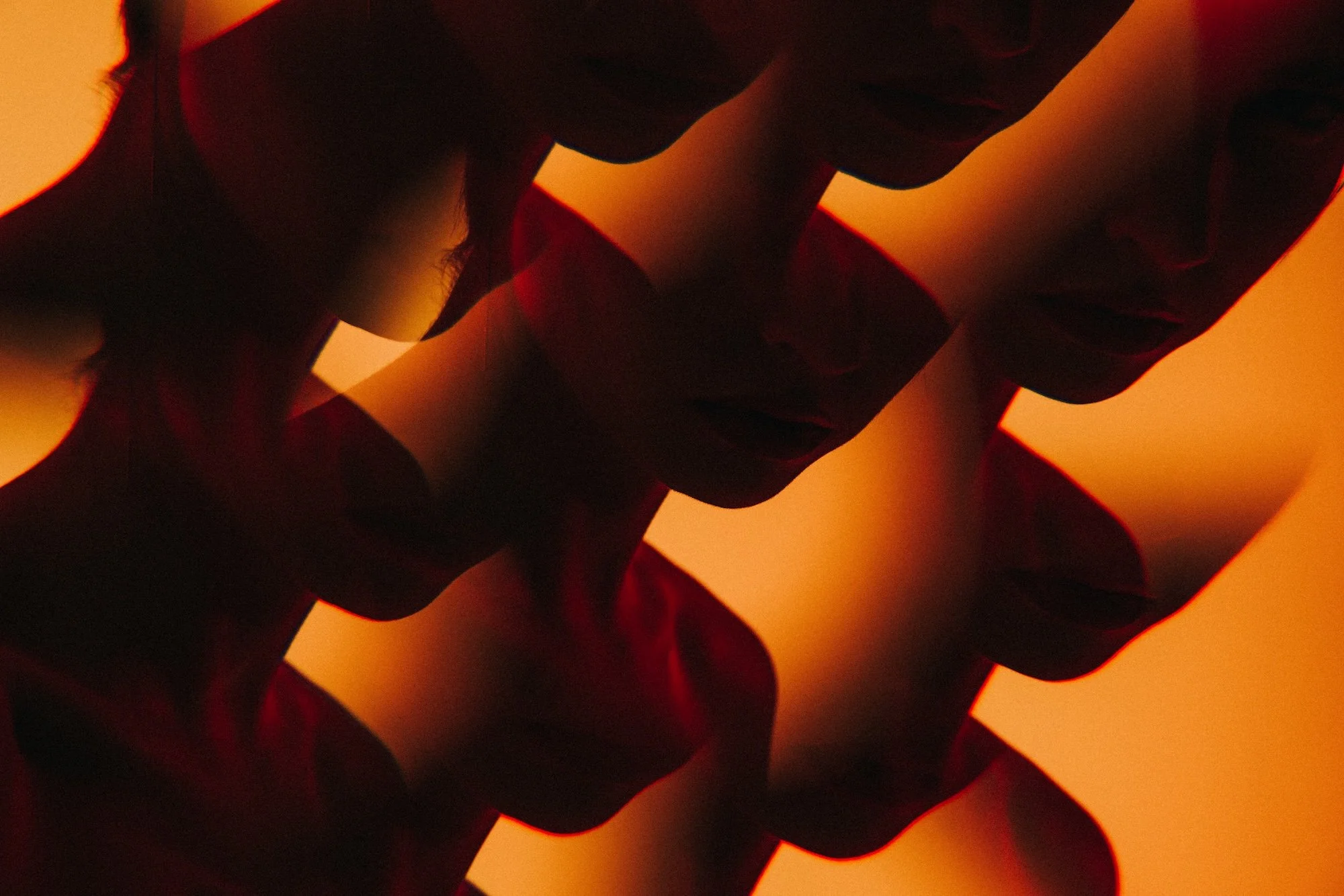 Close-up of a person with multiple overlapping faces with tinted red and orange lighting.