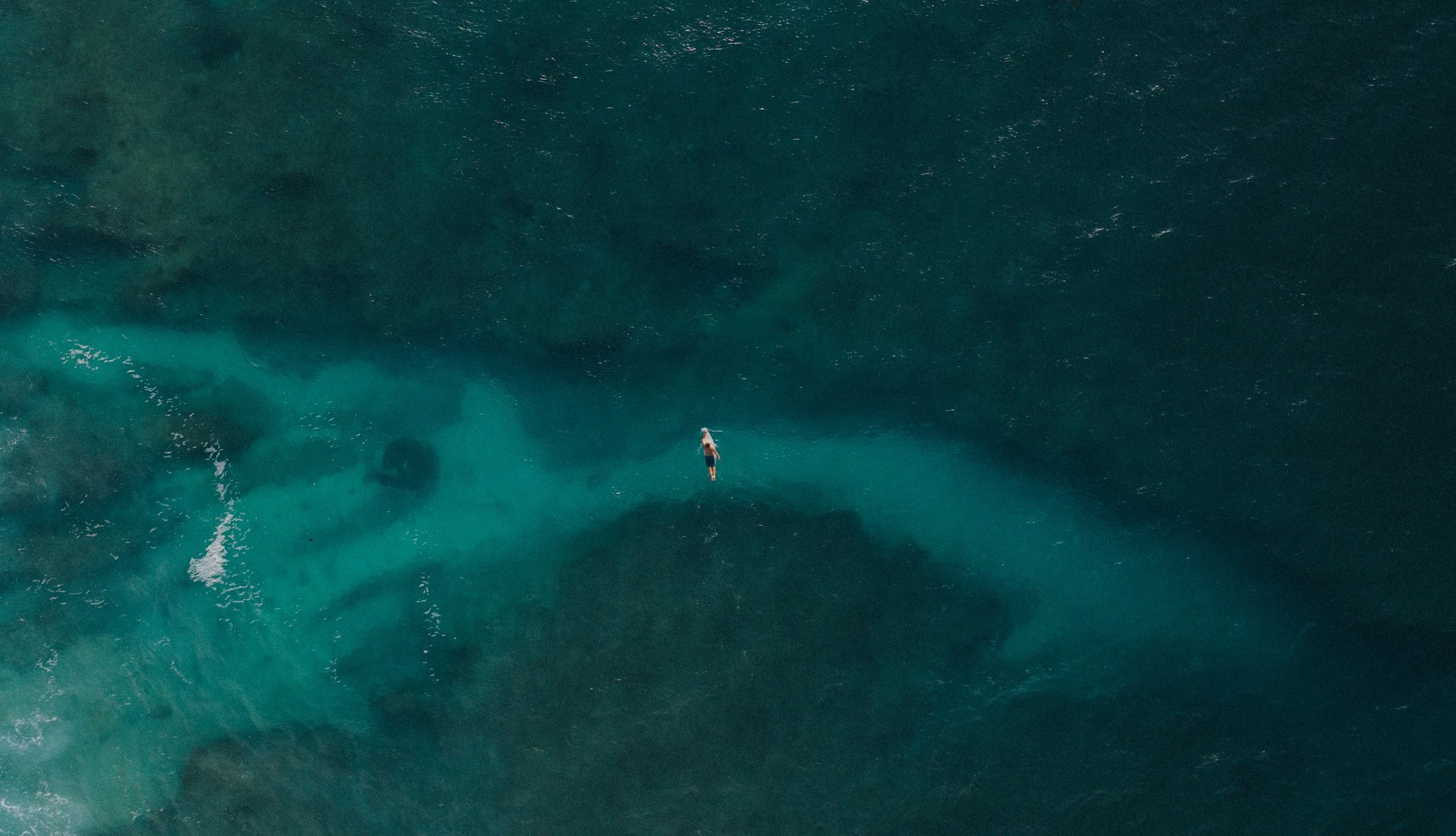 A person surfing on a wave in the ocean, seen from above.