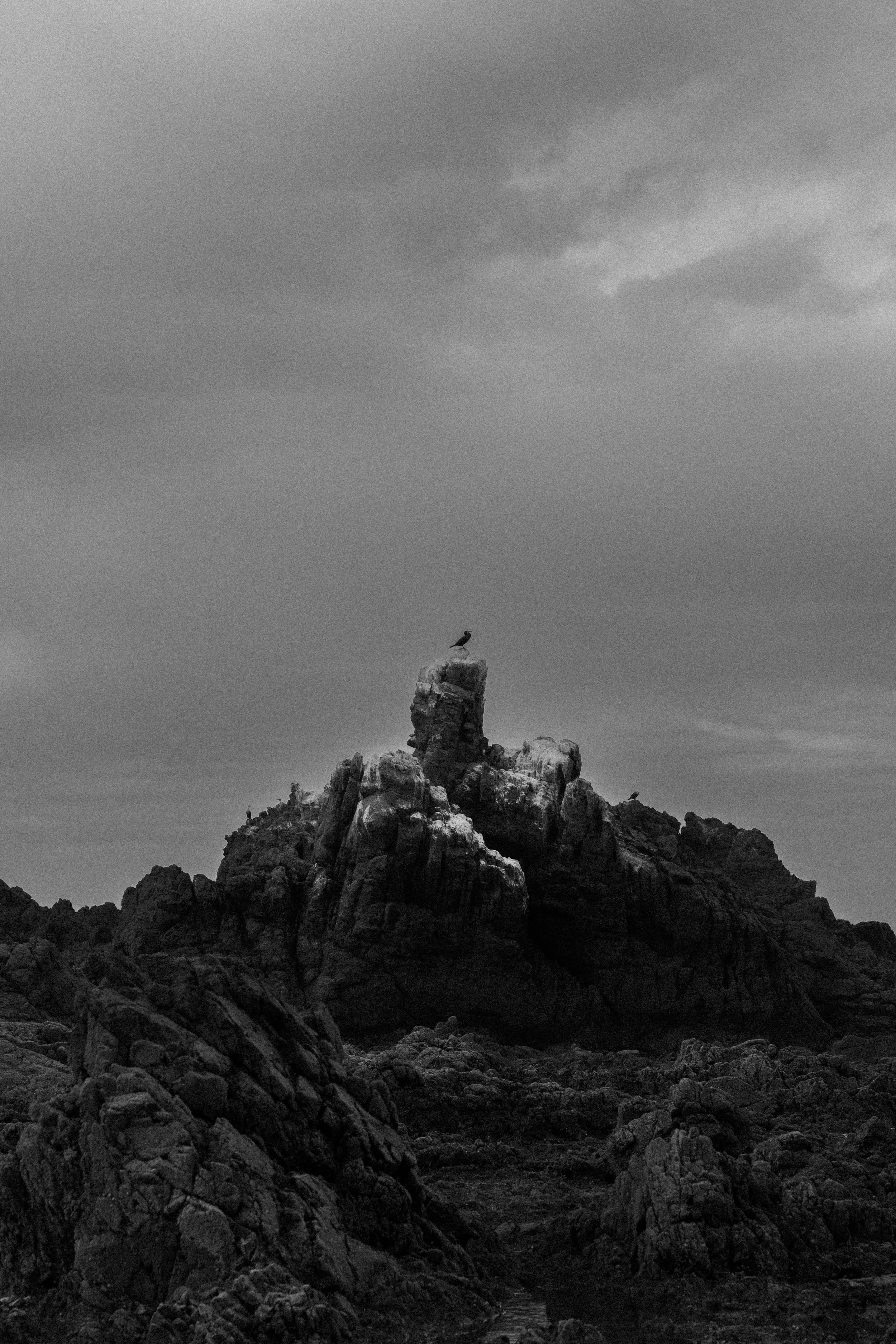 A rocky mountain with a bird perched on top, against a cloudy sky.