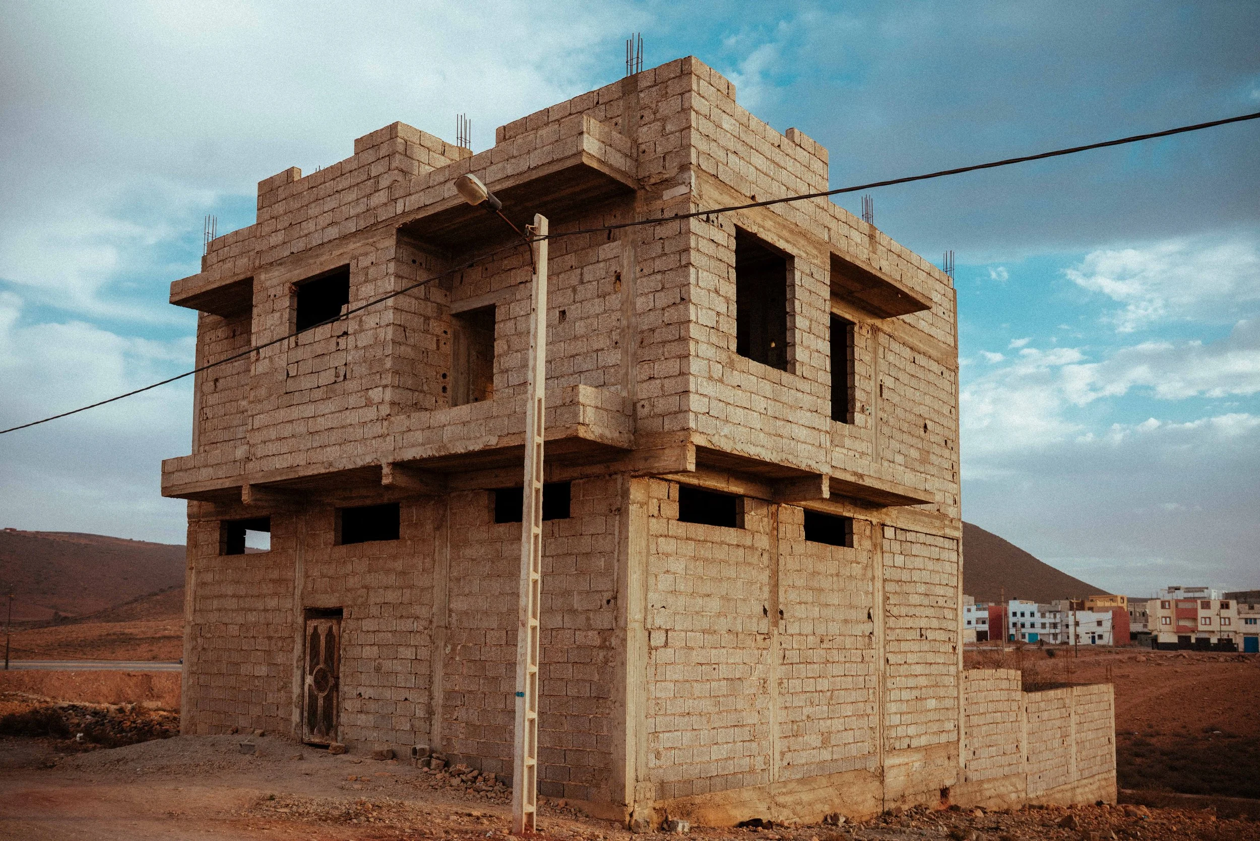 A multi-story brick building under construction in a semi-arid area with mountains in the background and a partly cloudy sky.