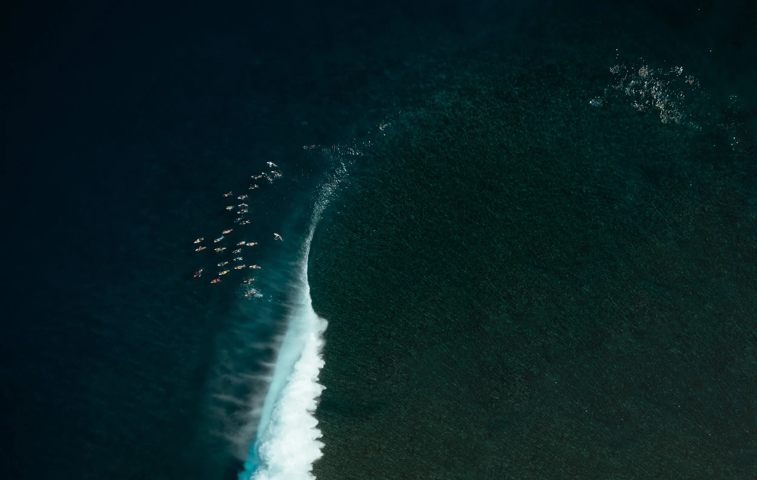 Aerial view of a surfer riding a large, powerful wave in the ocean with dark blue-green water.