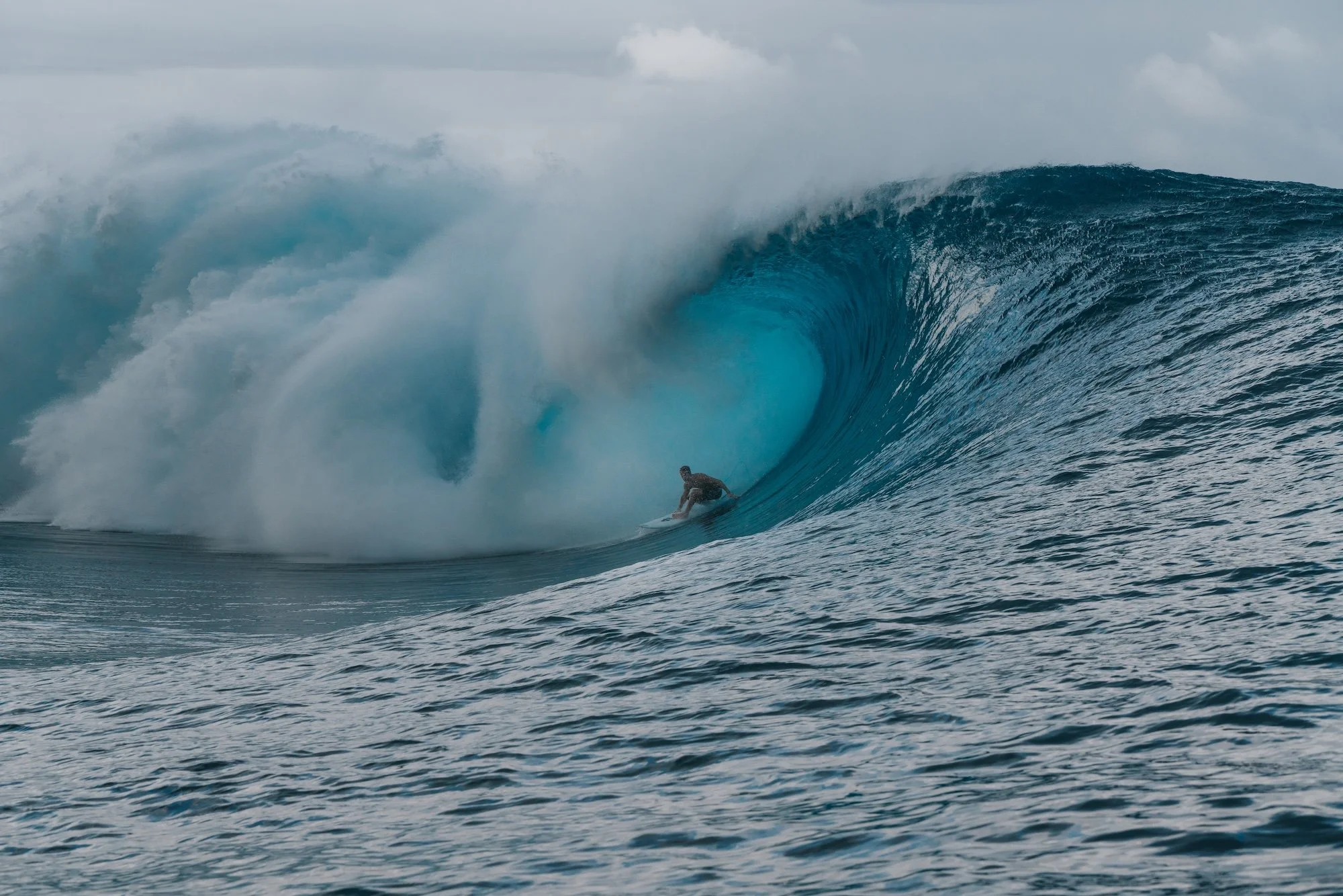 A person surfing a large blue wave in the ocean.