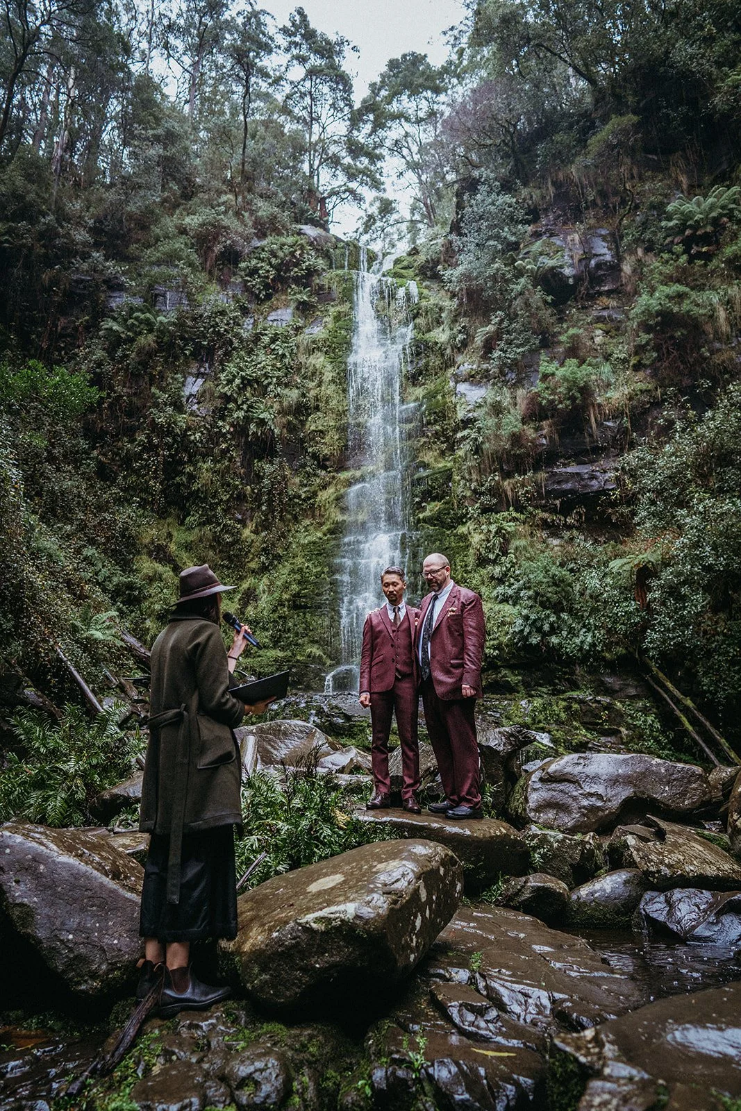 Couple embracing beside Erskine Falls during a rainy wedding ceremony