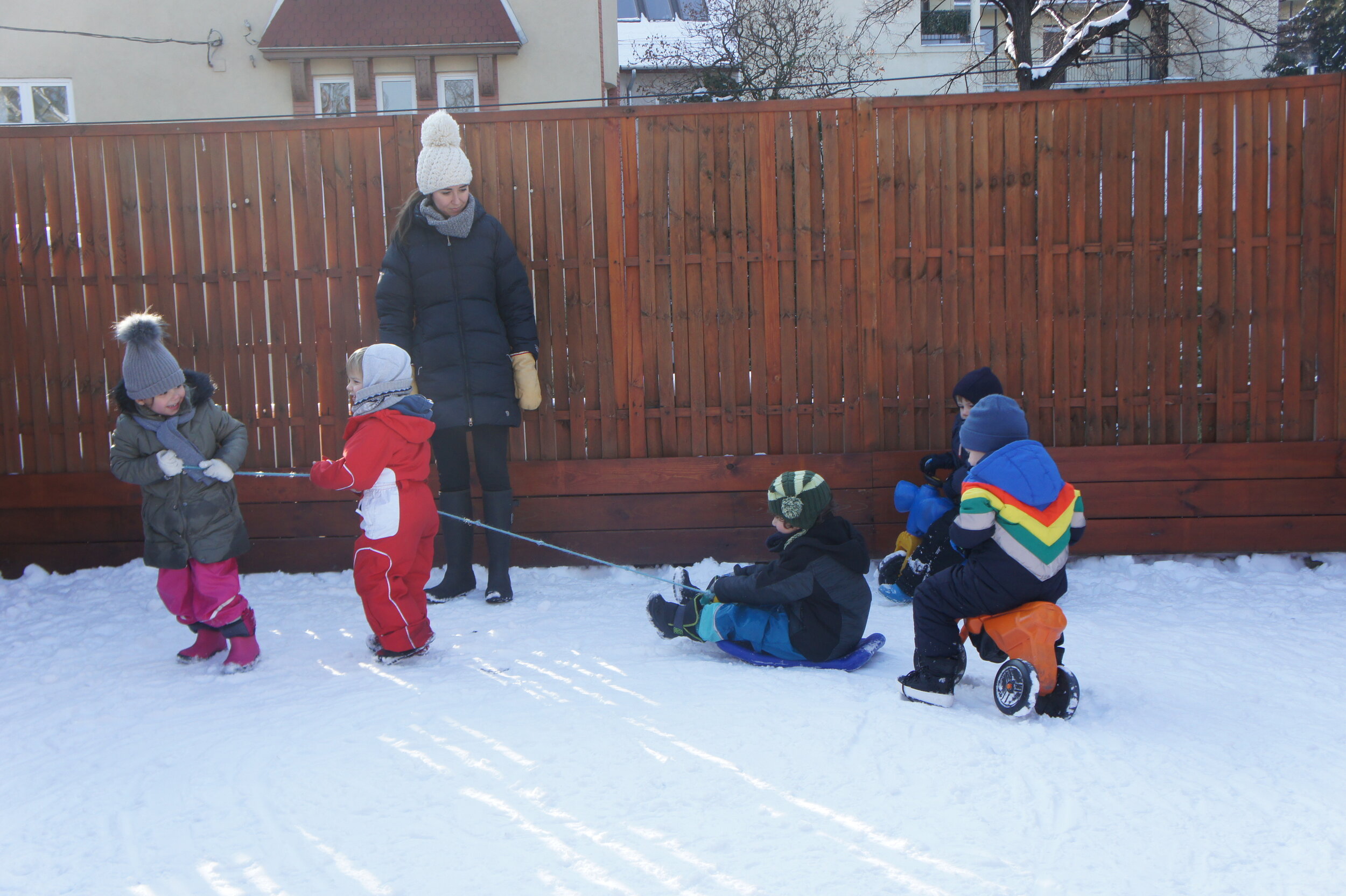 Children with Teacher Sledding Down the Snowy Hill in the Garden in Winter