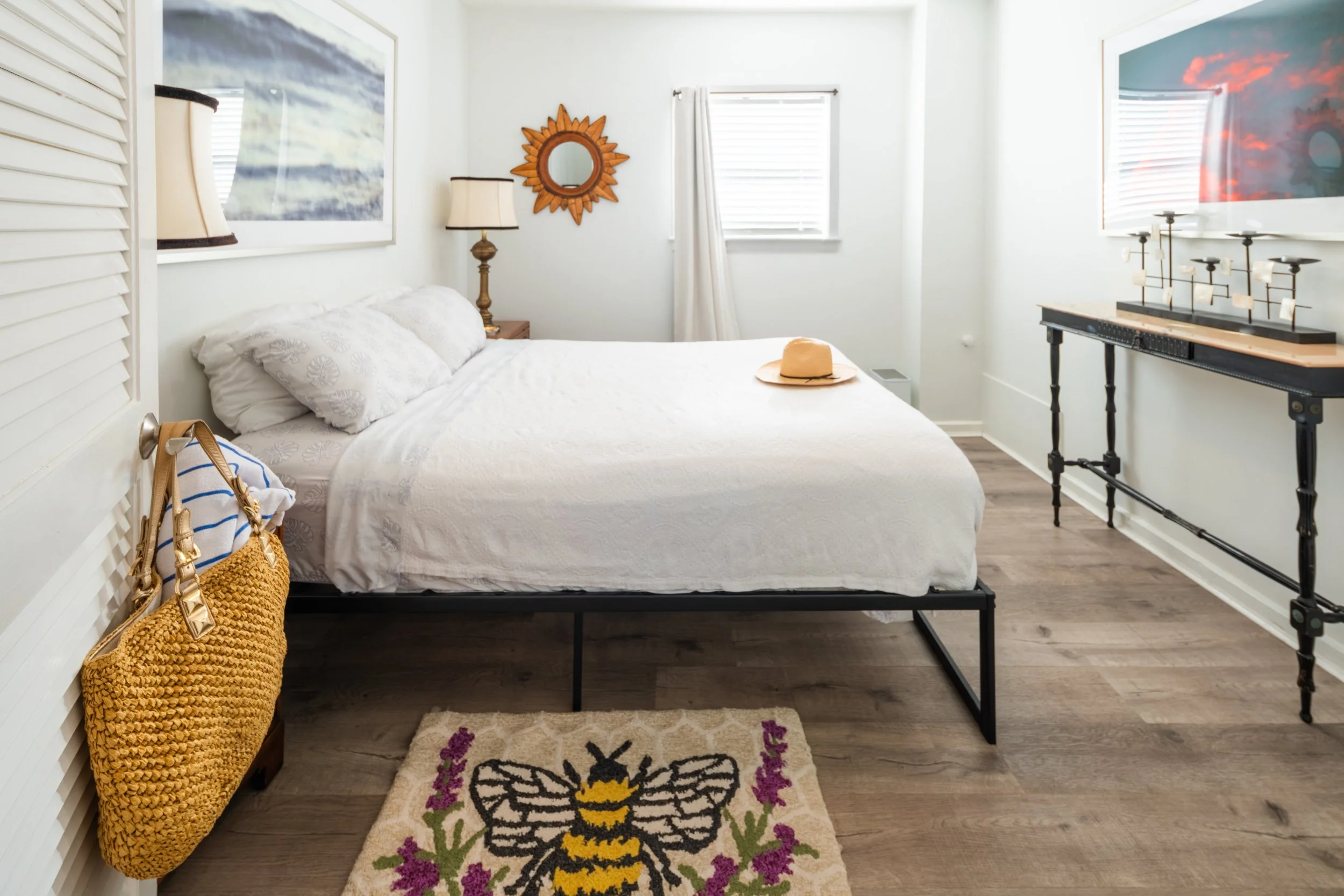 A white bed with pillows and a hat on it in a room with wood floors and artwork.