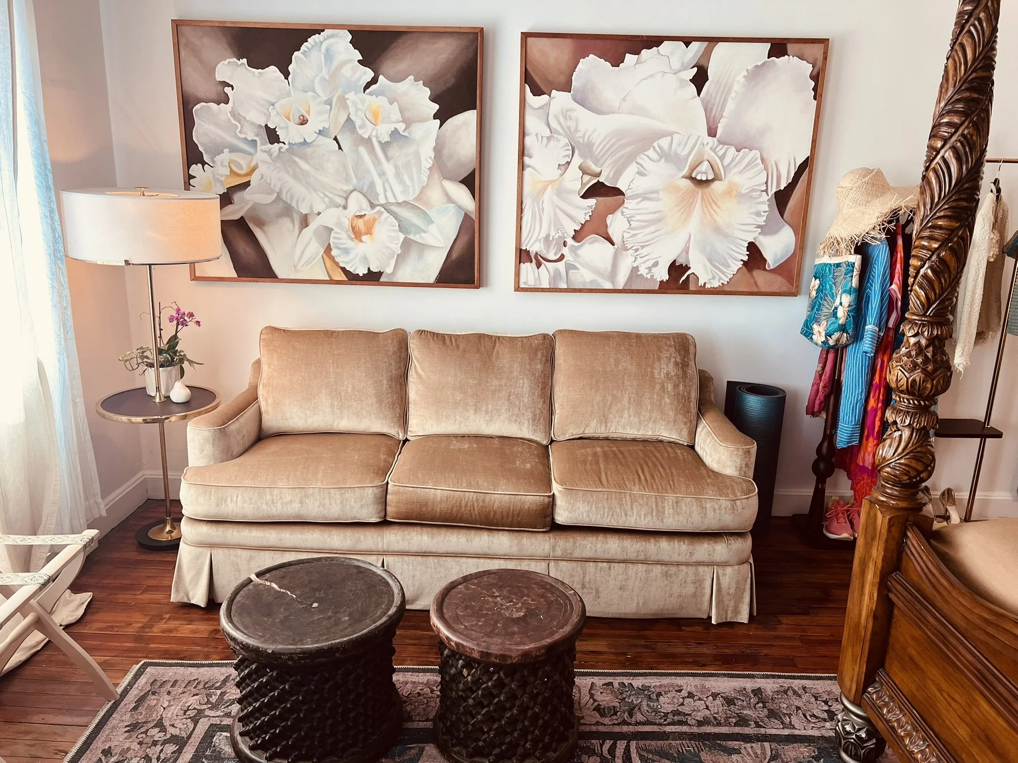 A cozy lobby with a beige couch, two wooden tables, and large floral artwork on the wall.