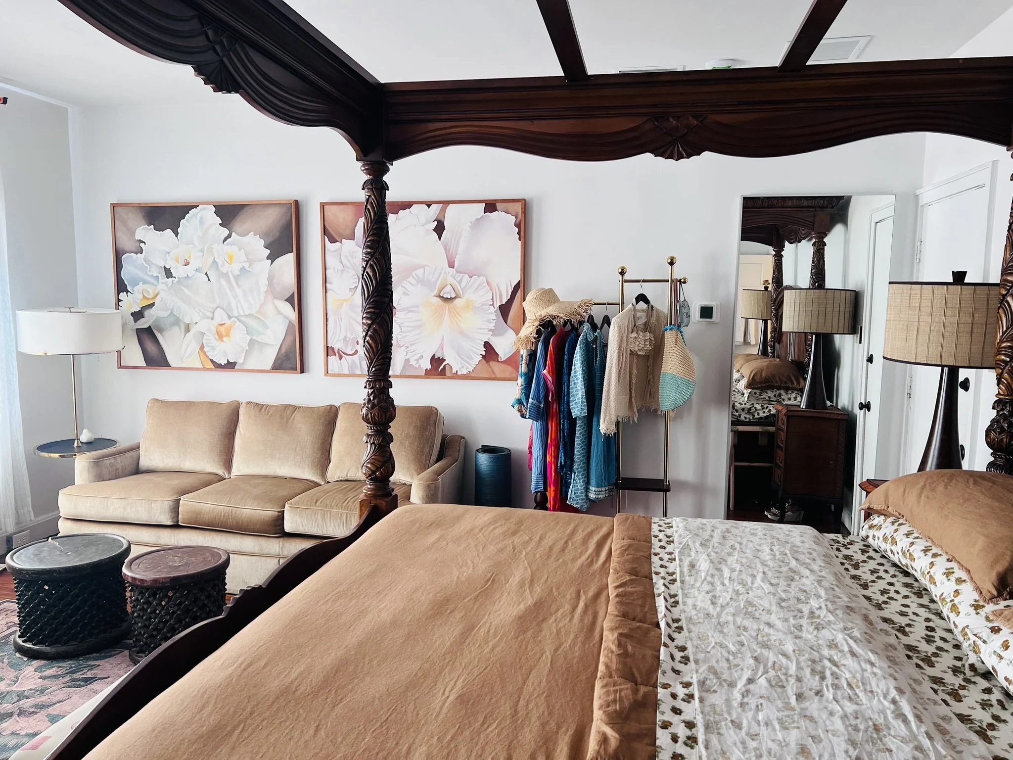 A luxurious hotel room with a four-poster bed, sofa, and large artwork.