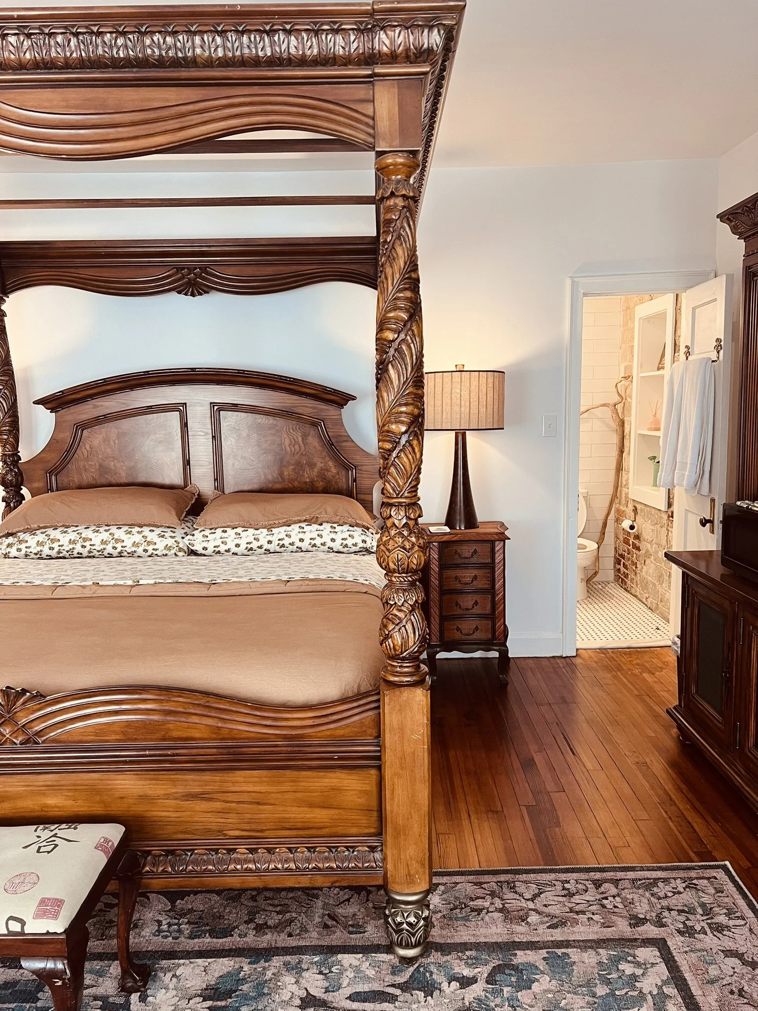 A bedroom with a four-poster bed, carved wooden furniture, and an open doorway to a bathroom.