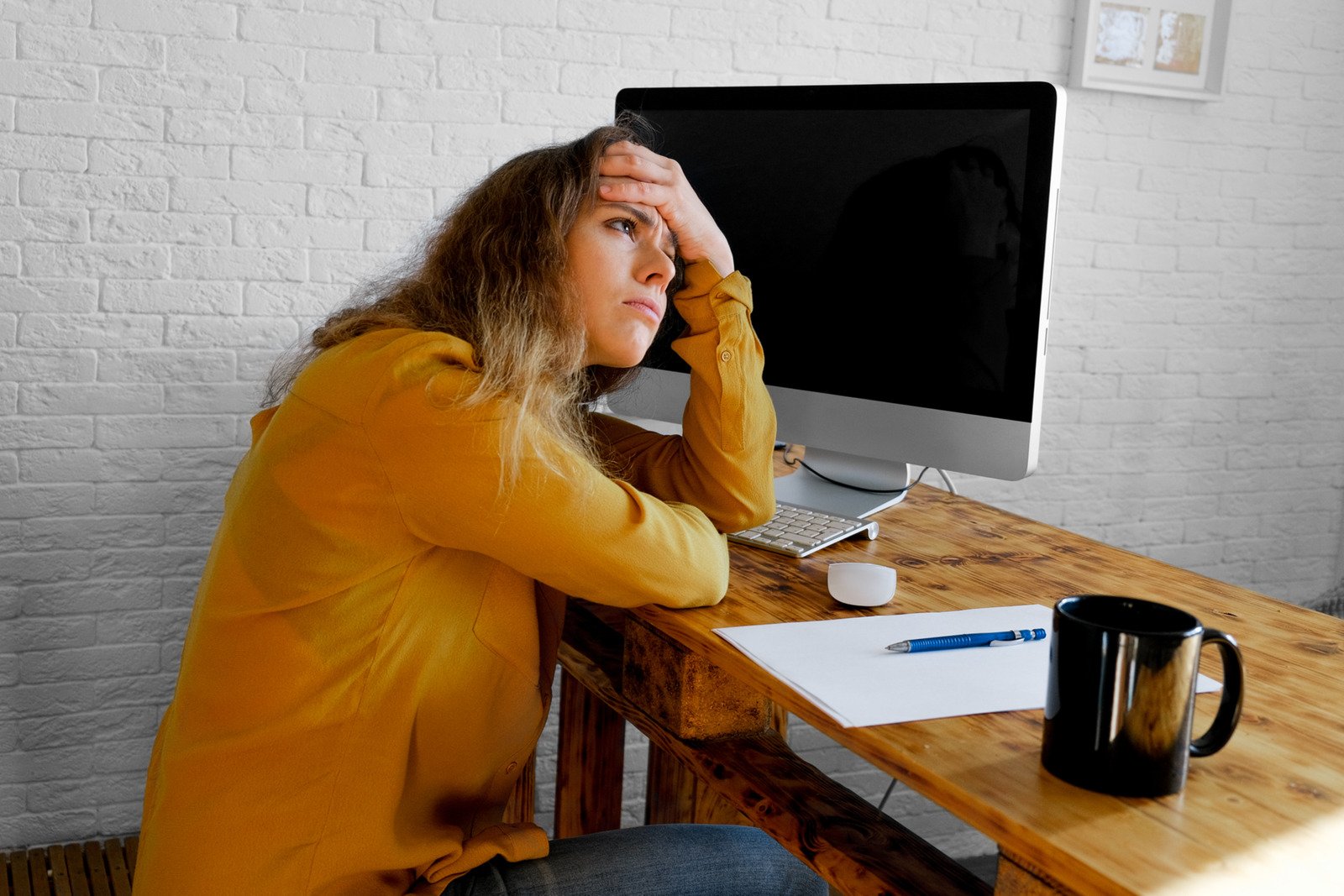 Tired, upset woman sitting at desk with a blank sheet of paper in front of her.