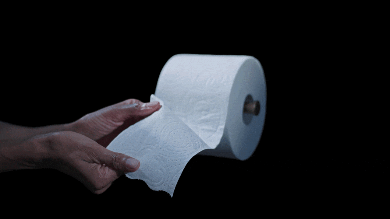 A person holding a roll of white toilet paper against a black background.