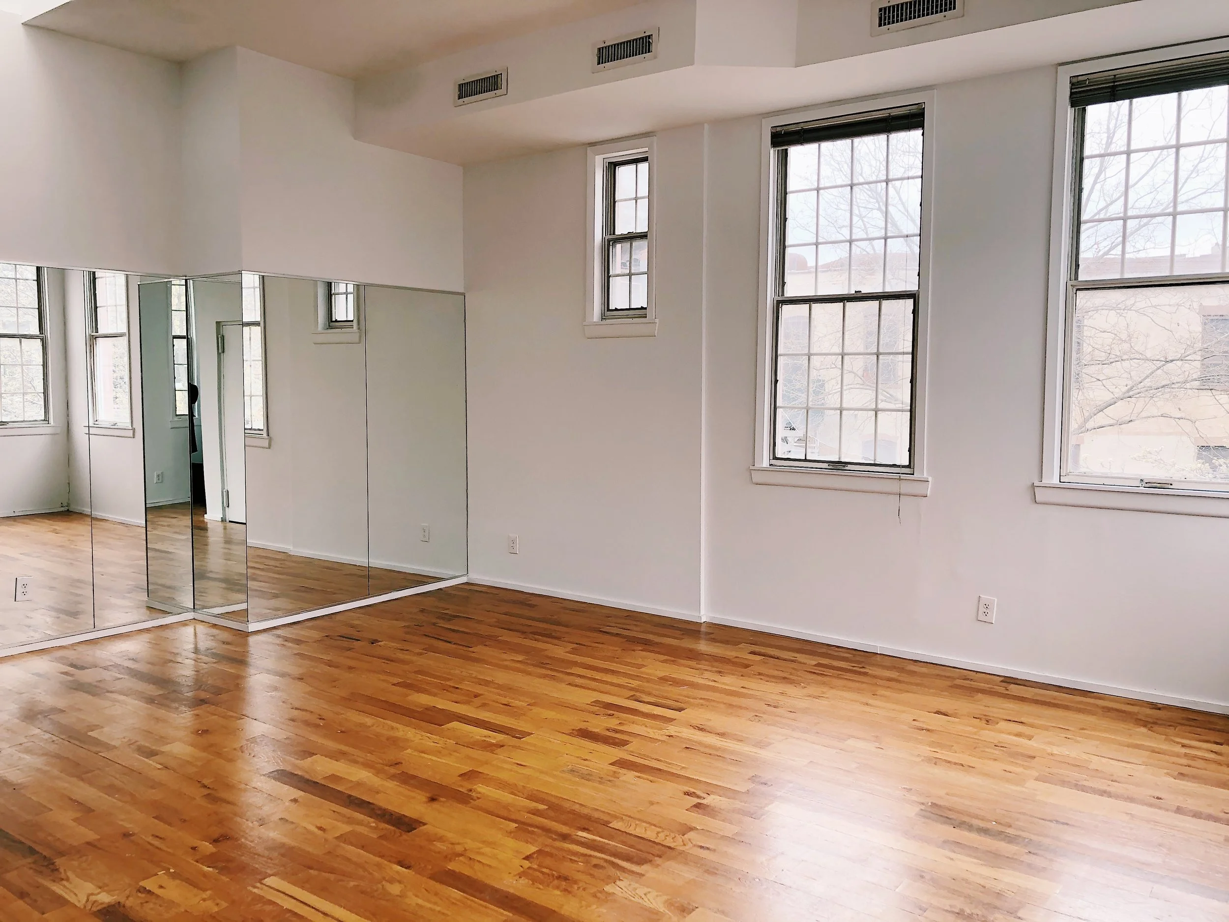 Stu studio with white floors, a mirror, windows and hardwood floors.