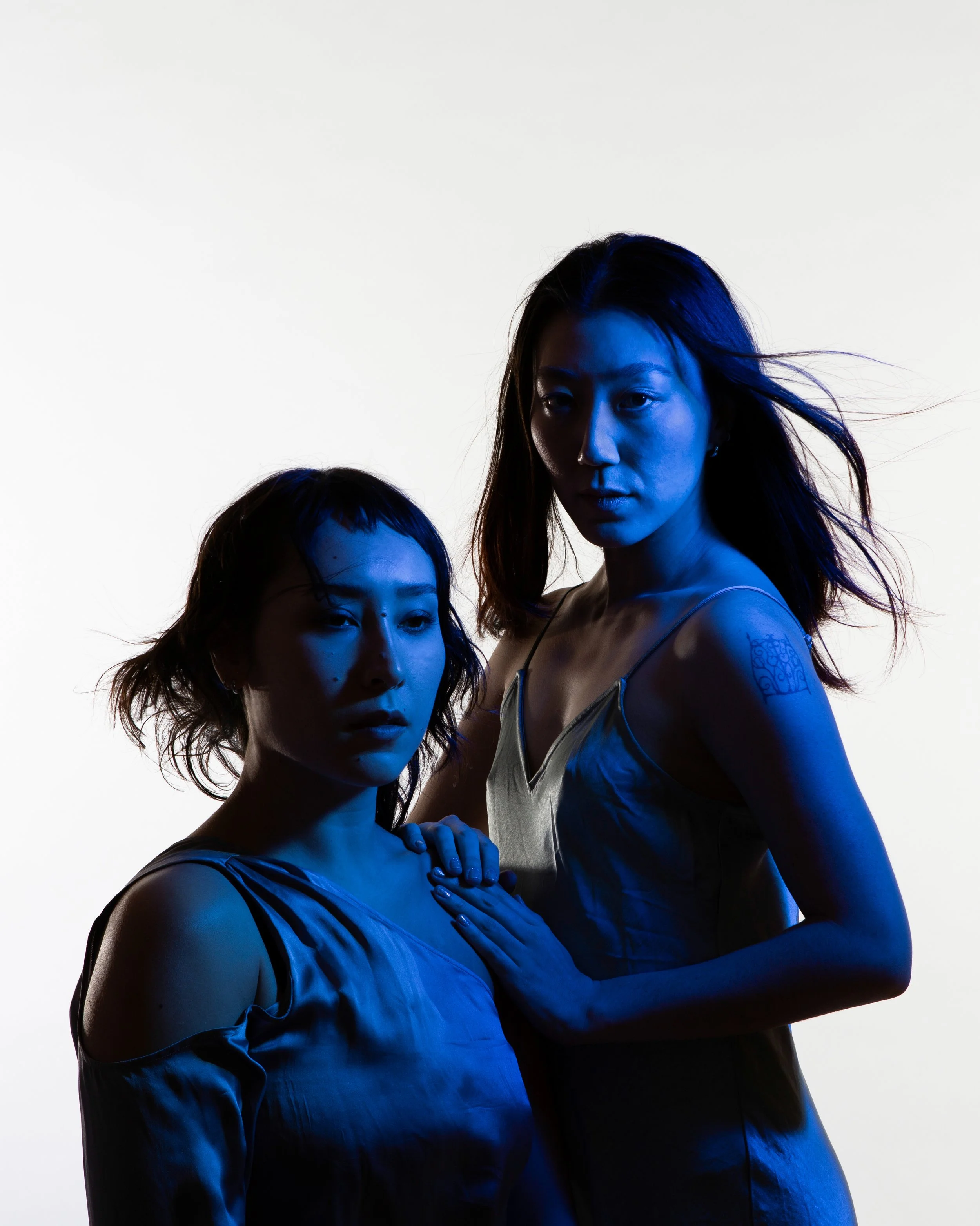 Kimie Parker and kira shiina link arms and pose angularly with a blue background.