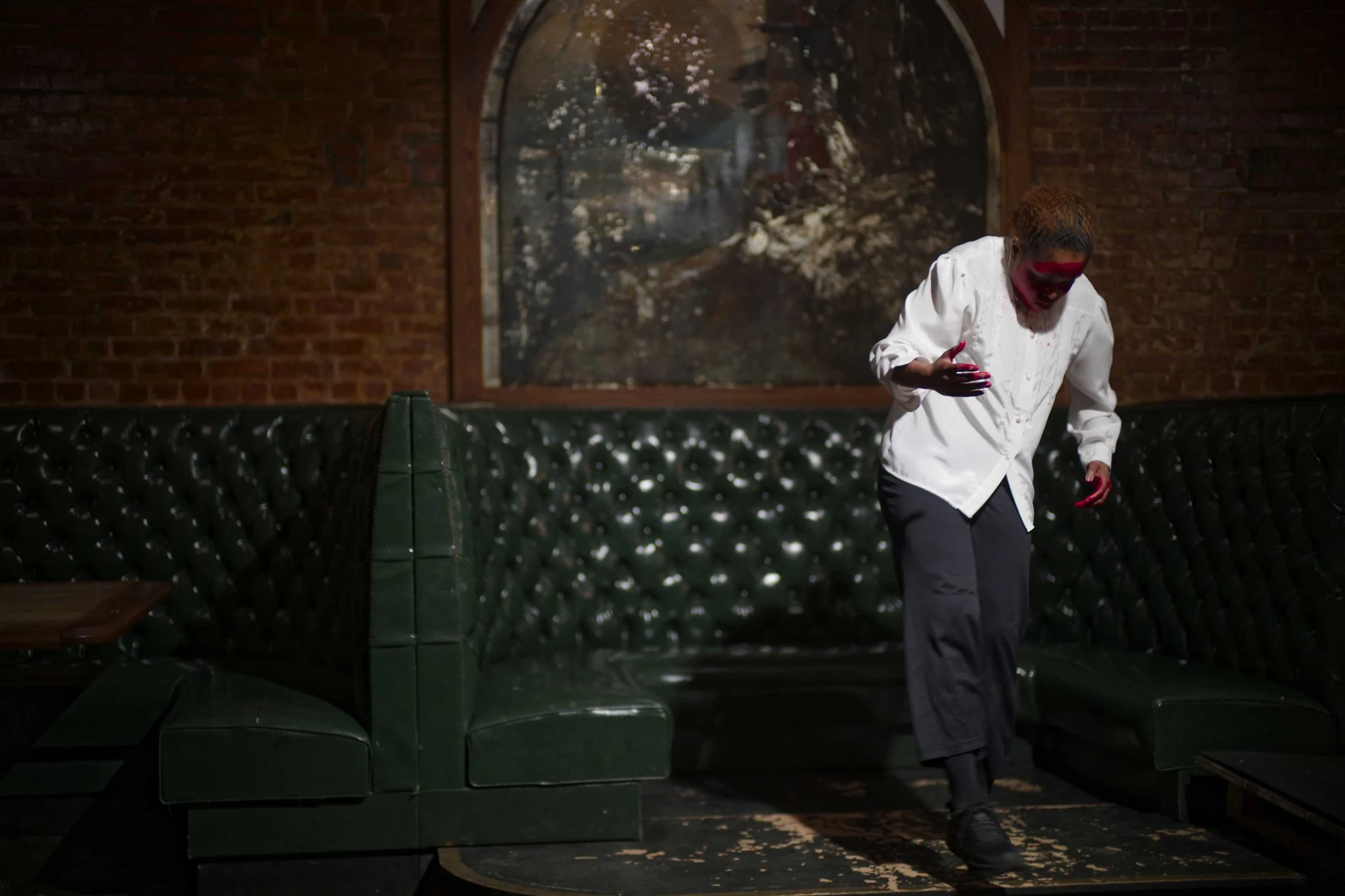 Bryanna Stickland steps down off a platform in a bar. She wears a white t-shirt with red paint on her hands and face.