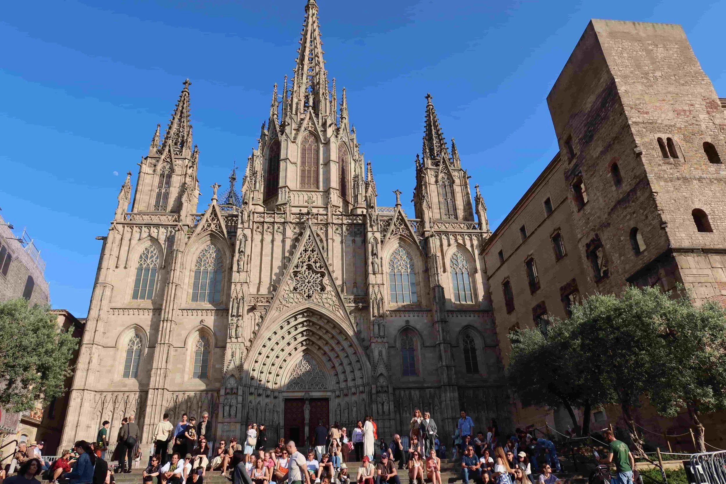 big gothic cathedral in barcelona with lots of people blue sunny day