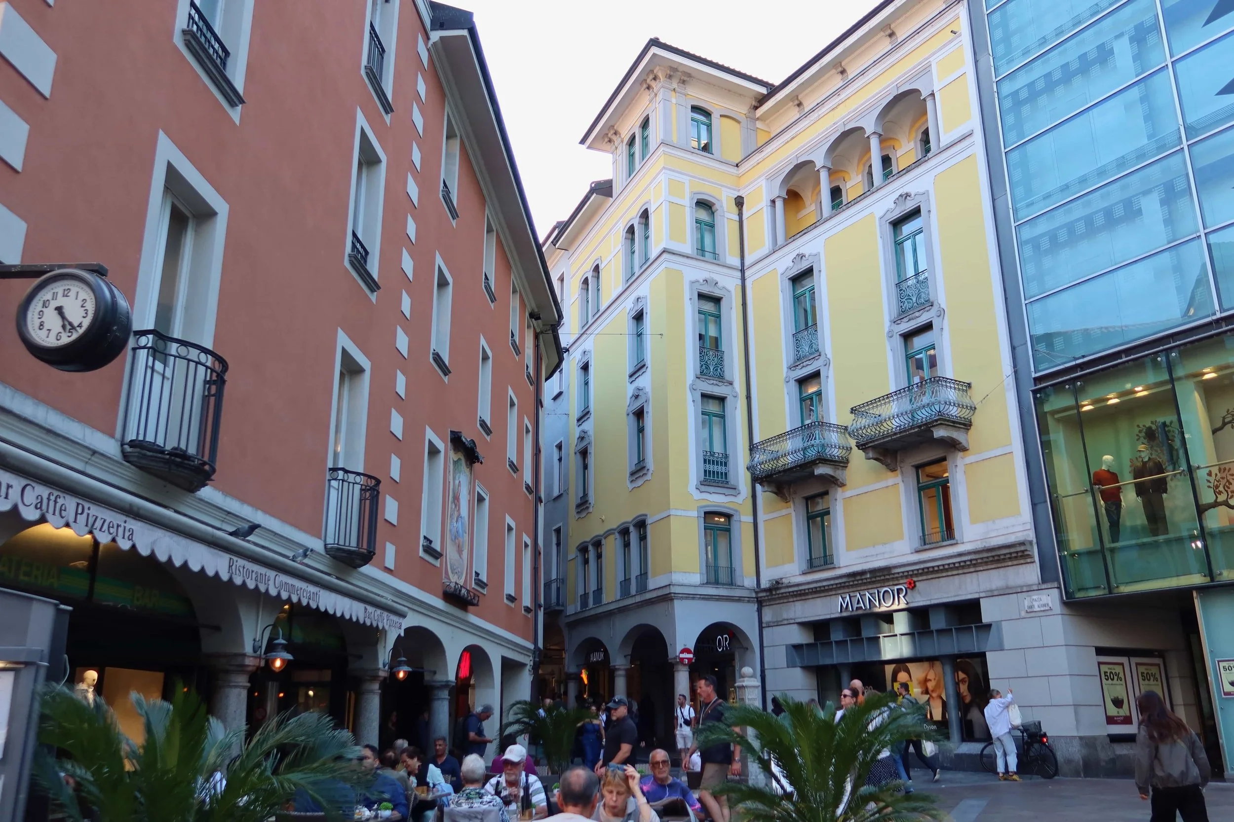 local scquare with orange and yellow buildings with pizzeria and people