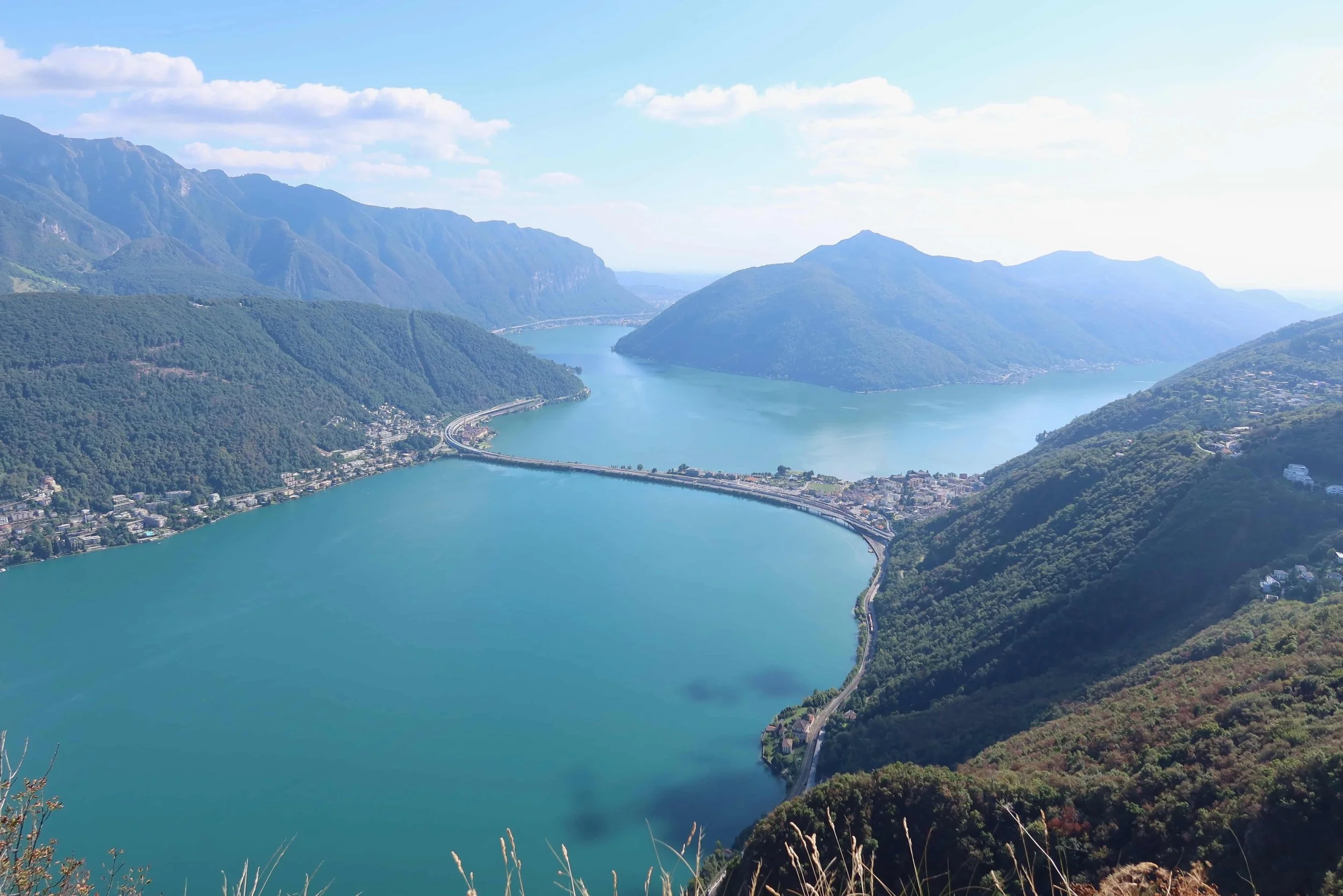 teal water and bridge in between lucious green mountains with milan in the distance