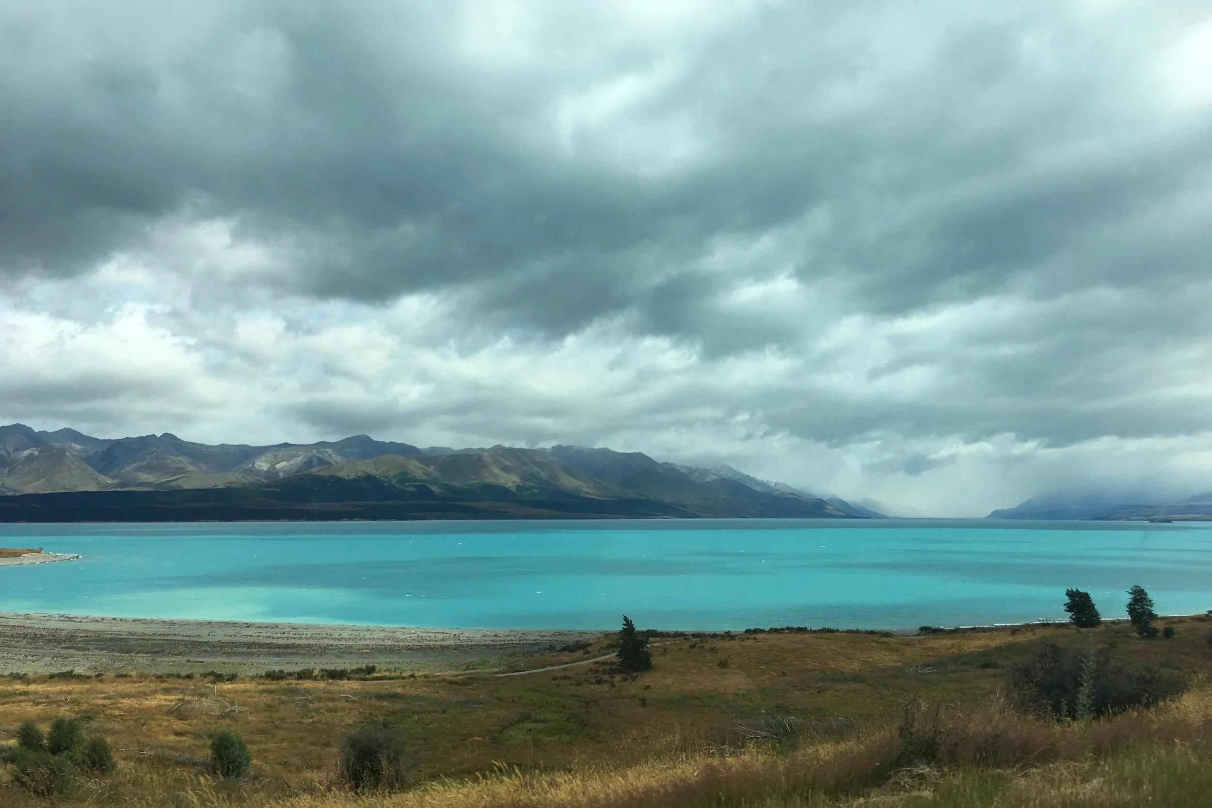teal water with mountains and cloudy sky