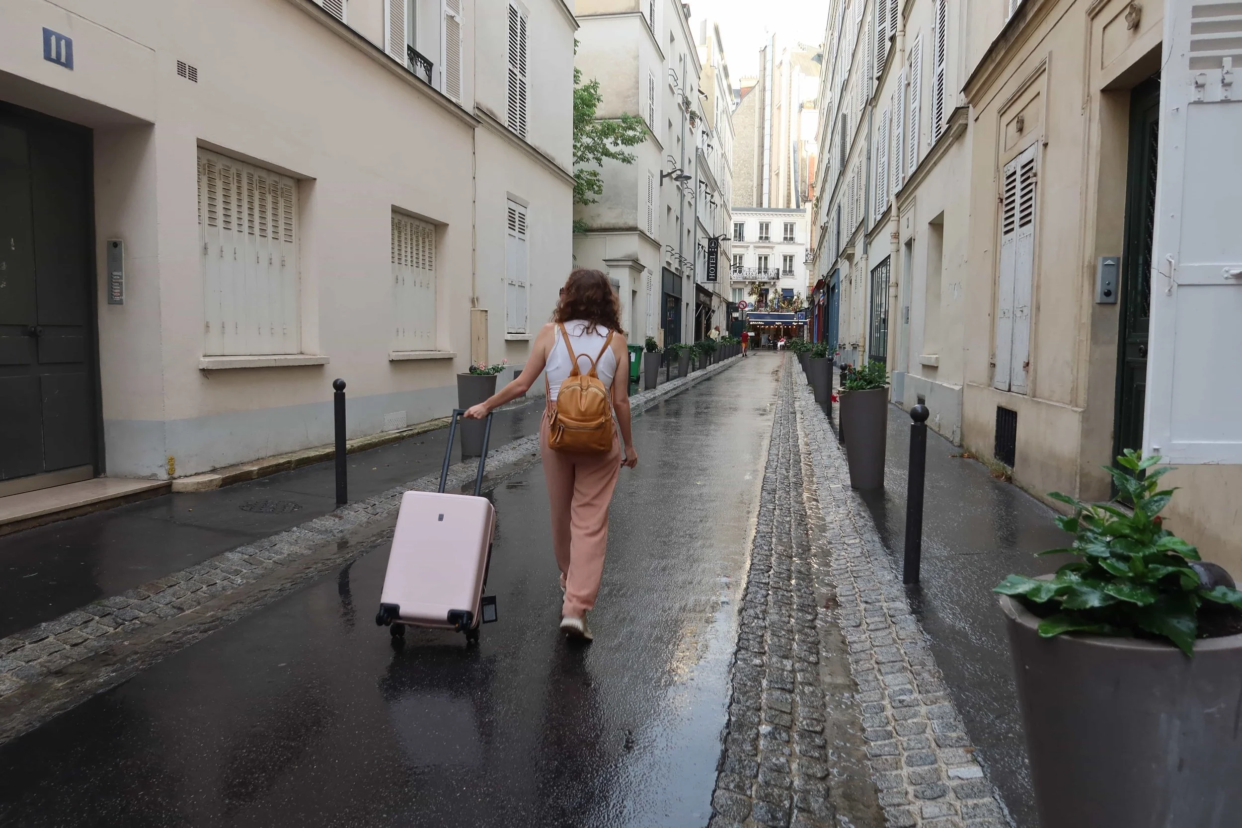 girl with tan backack walking with light pink suitcase