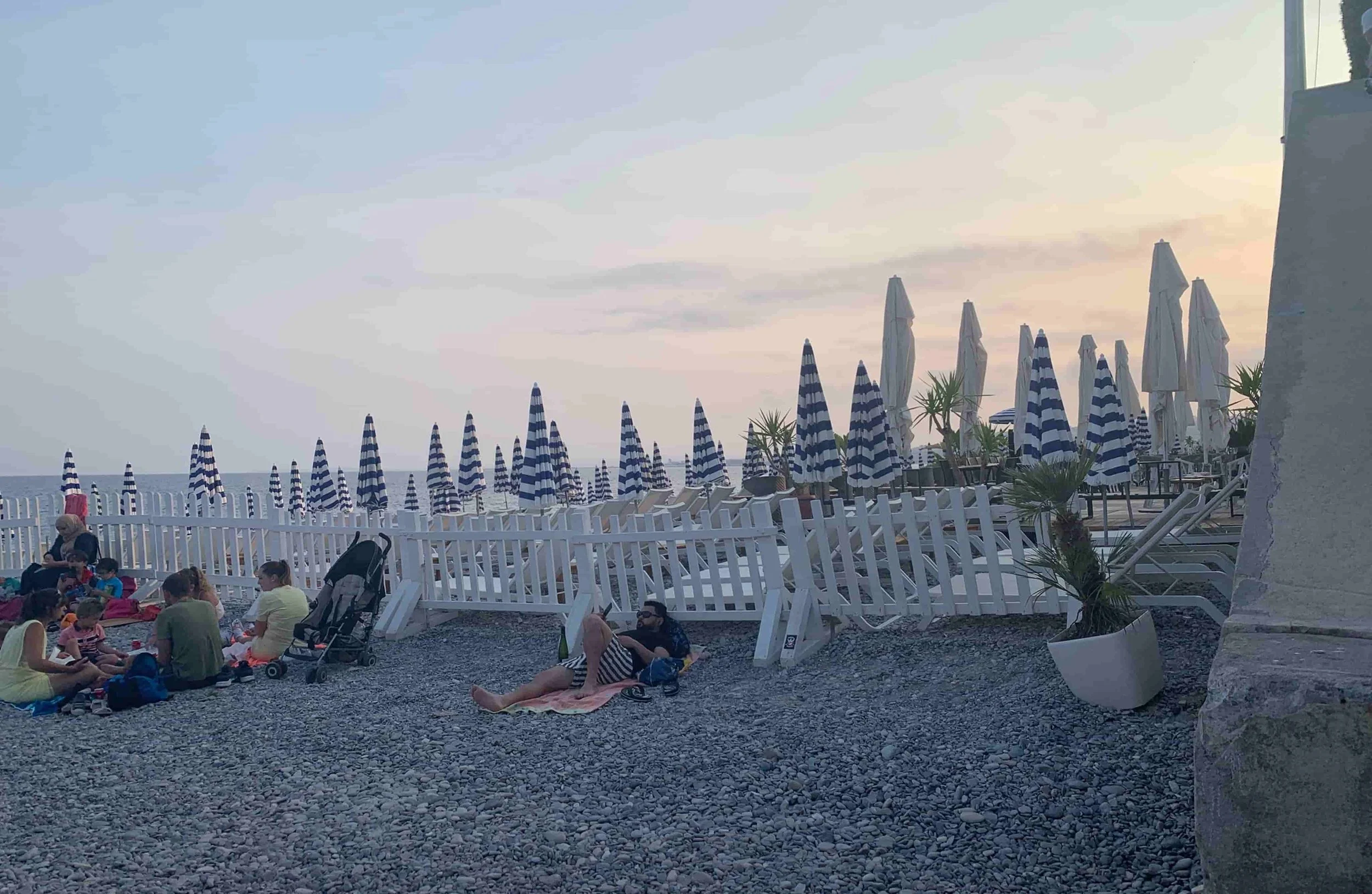 people laying on pebbles near blue and white beach chairs
