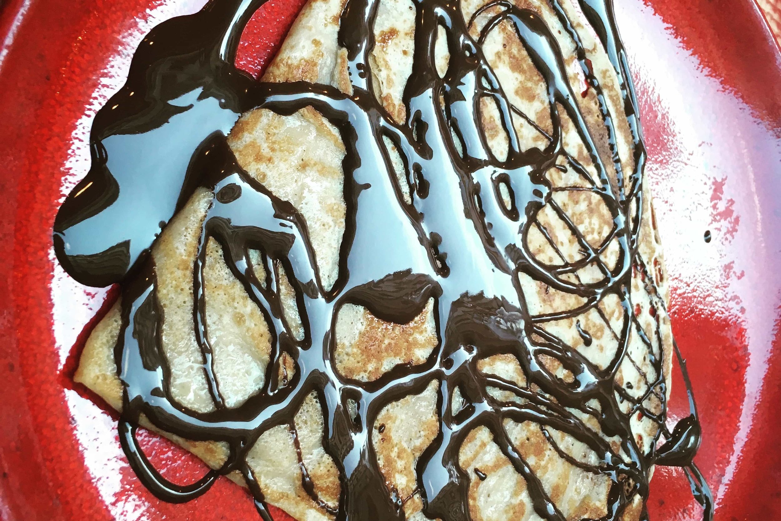 crepe on red plate with chocolate syrup