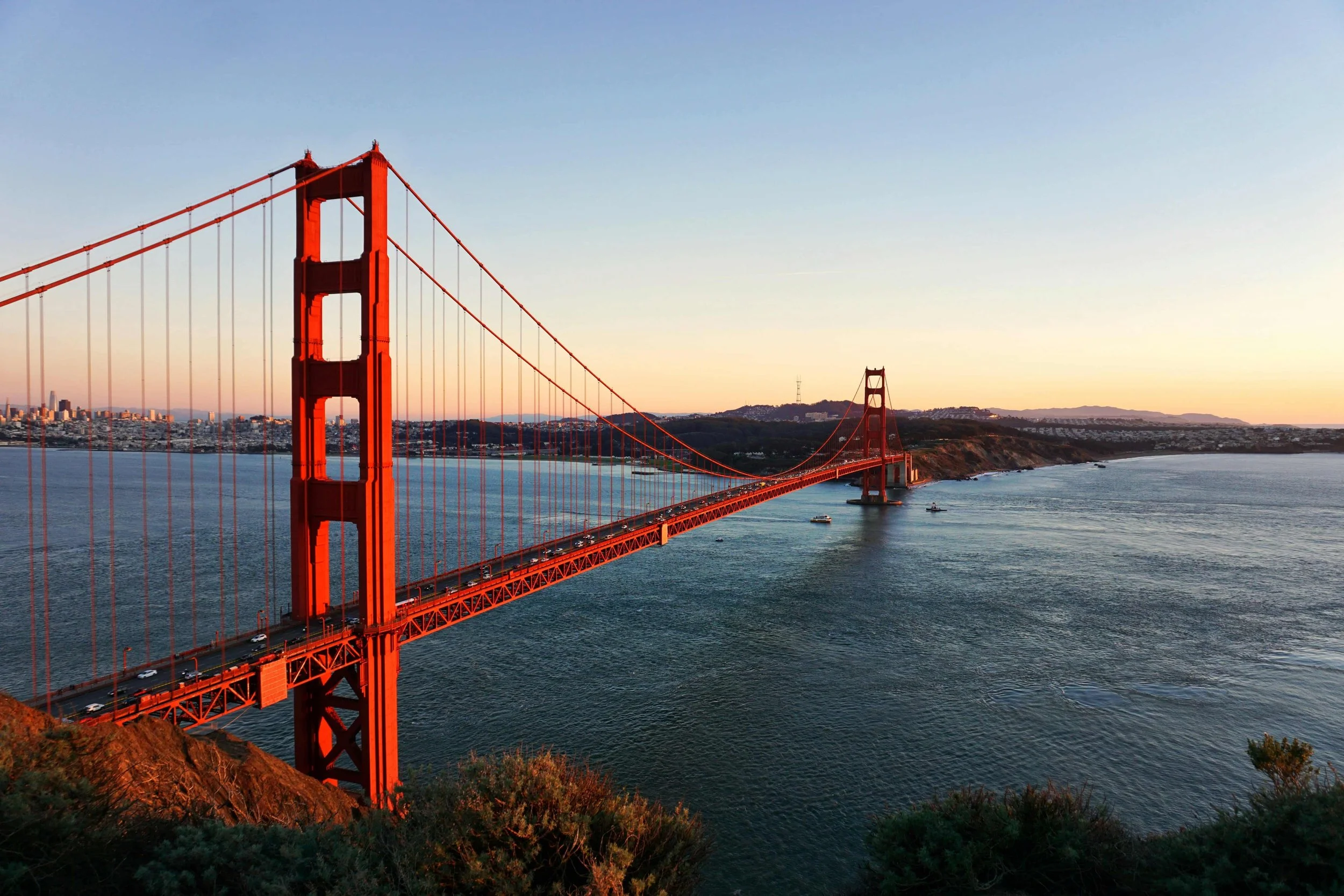 red bridge with tall towers and sunset on water