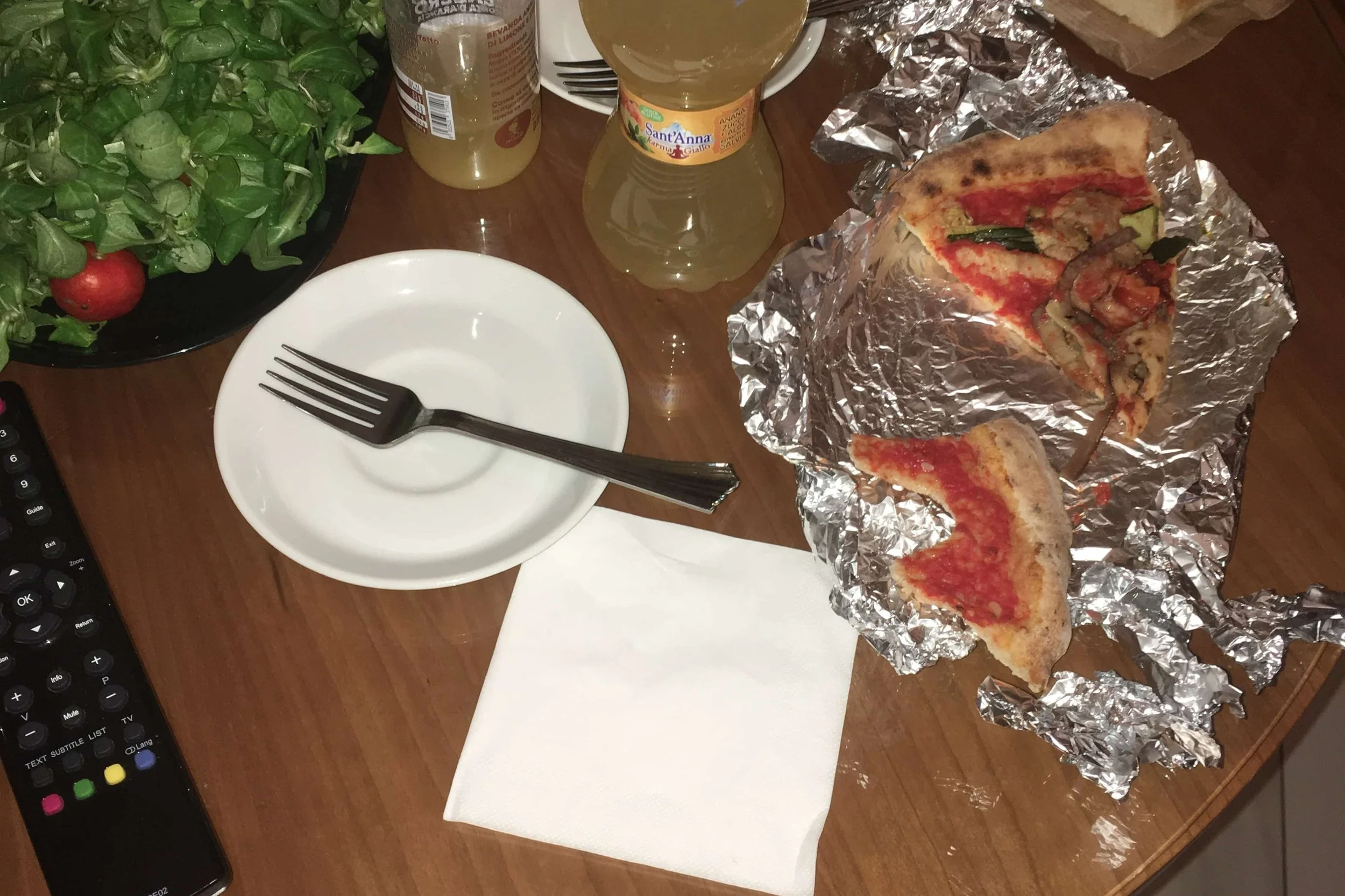 left over pizza in tin foil with tv remote on hotel table