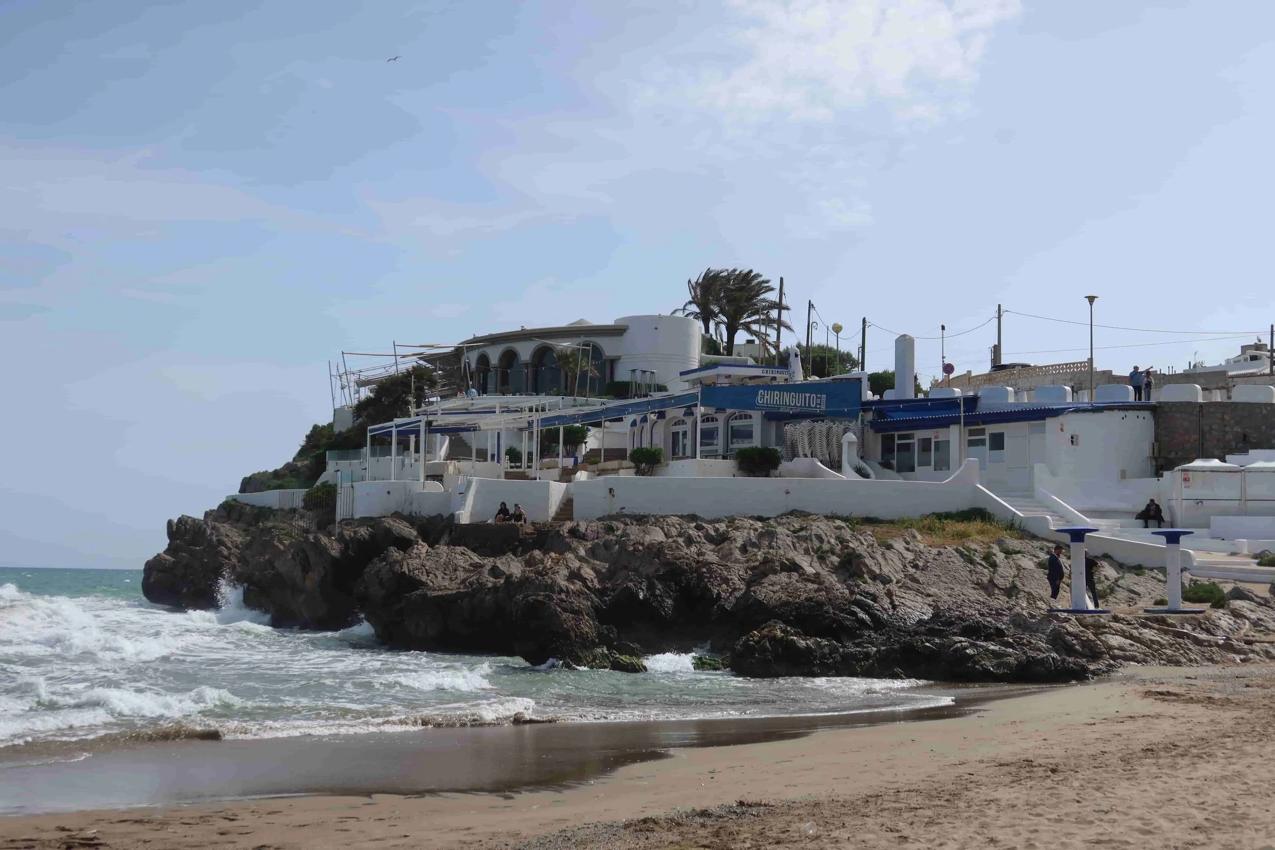white and blue restaraunt on beach cliff ocean and sand on sunny day