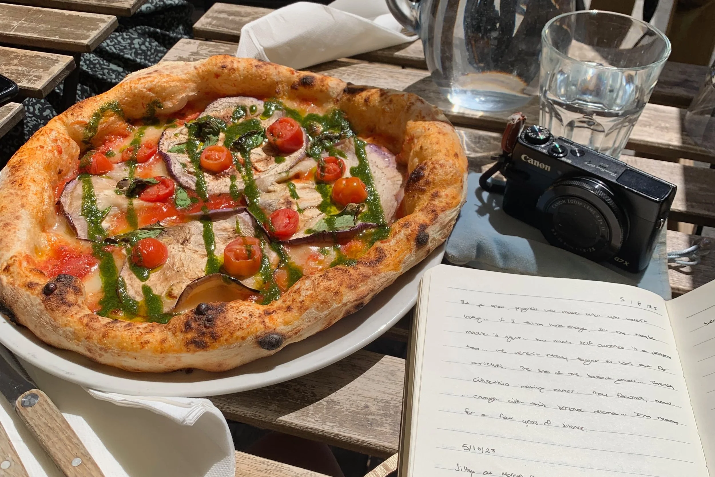 pizza with eggplant tomatoes basil and journal with camera on table