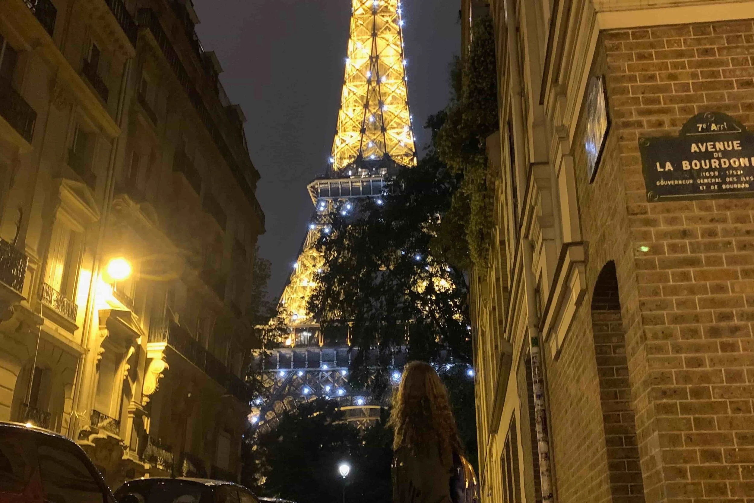 girl standing underneath eiffel tower sparkling at night
