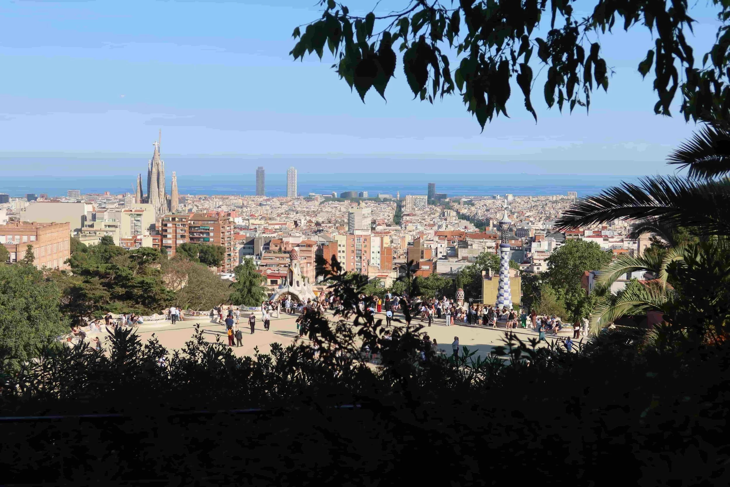shady view of parc guell blue spire church and ocean ahead