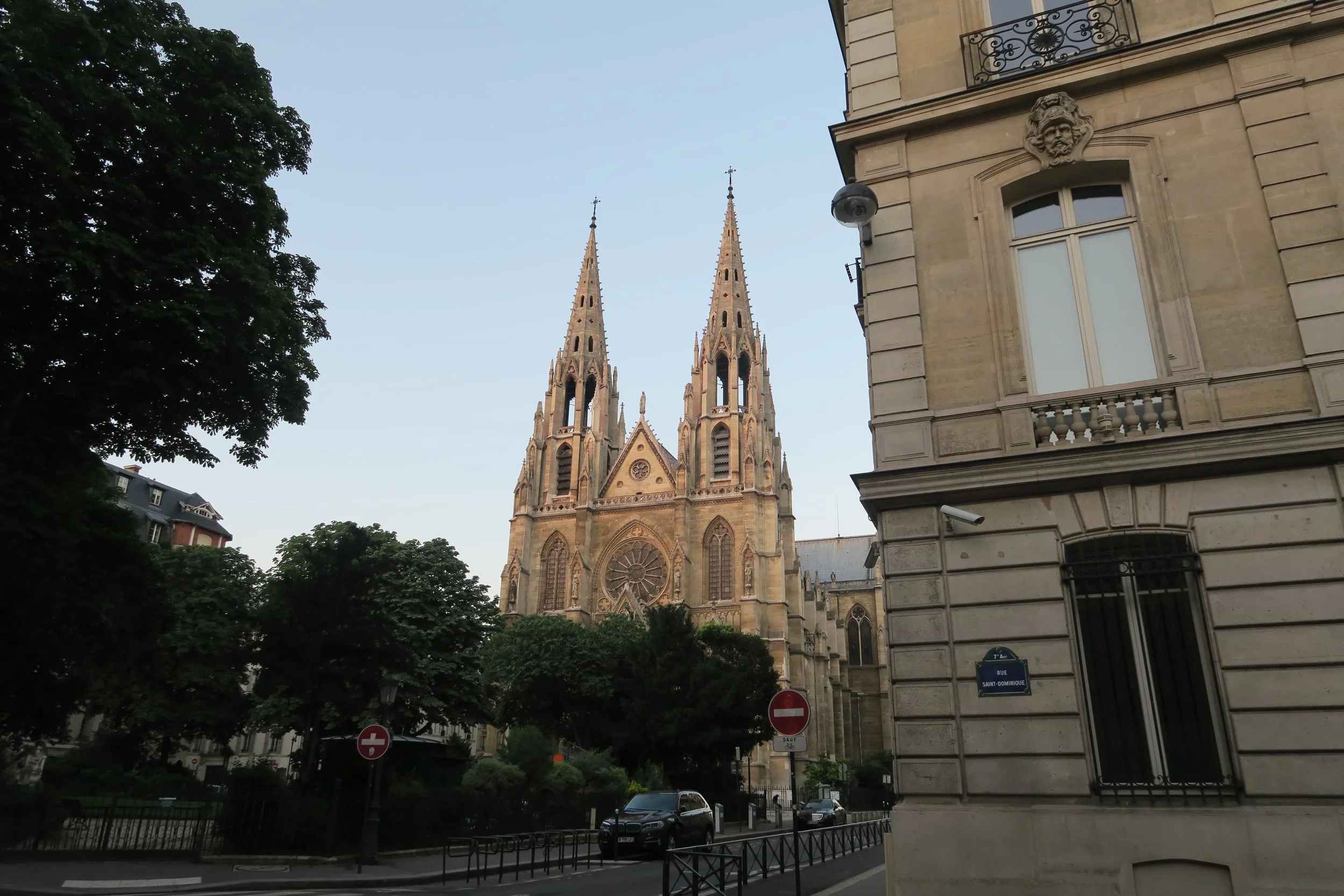 church with light brown spires and pale skies and big leafy green tree