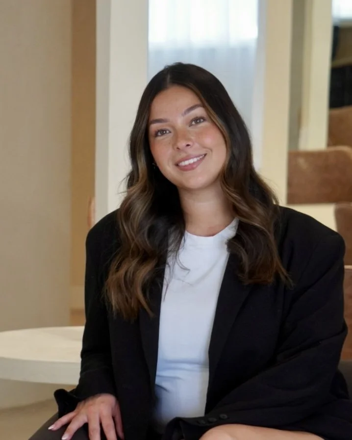 A woman with dar brown hair in a white shirt and black blazer smiling at the camera