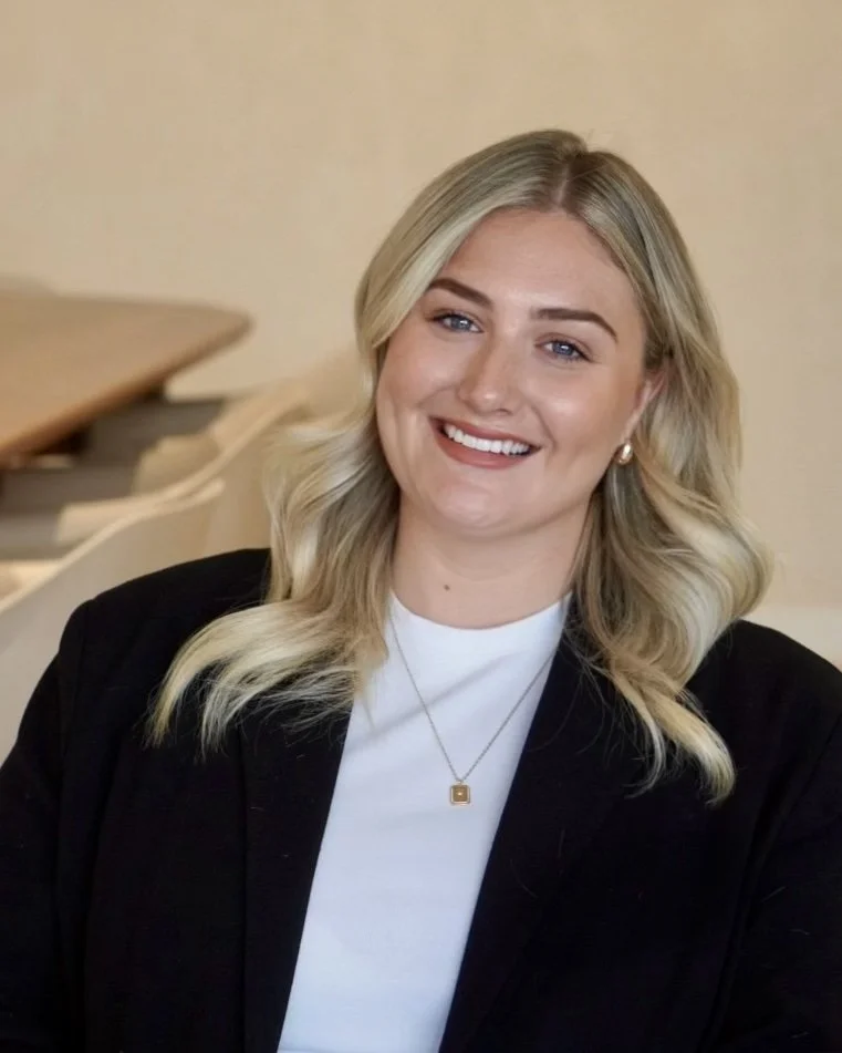 A woman with blonde hair in a white shirt and black blazer smiling at the camera