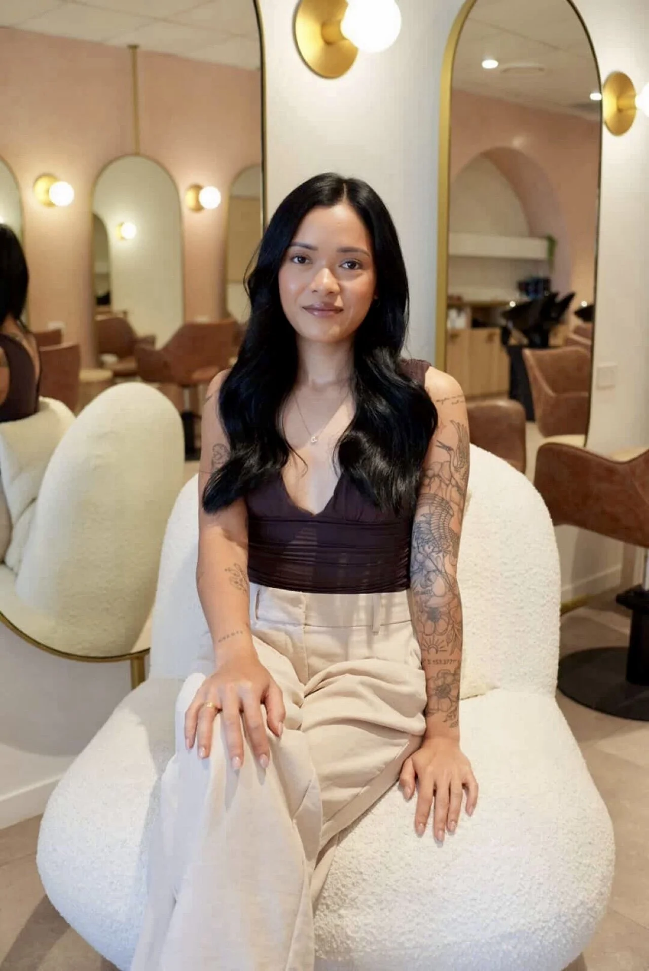 Woman with dark hair sitting on a white chair inside of a hair salon