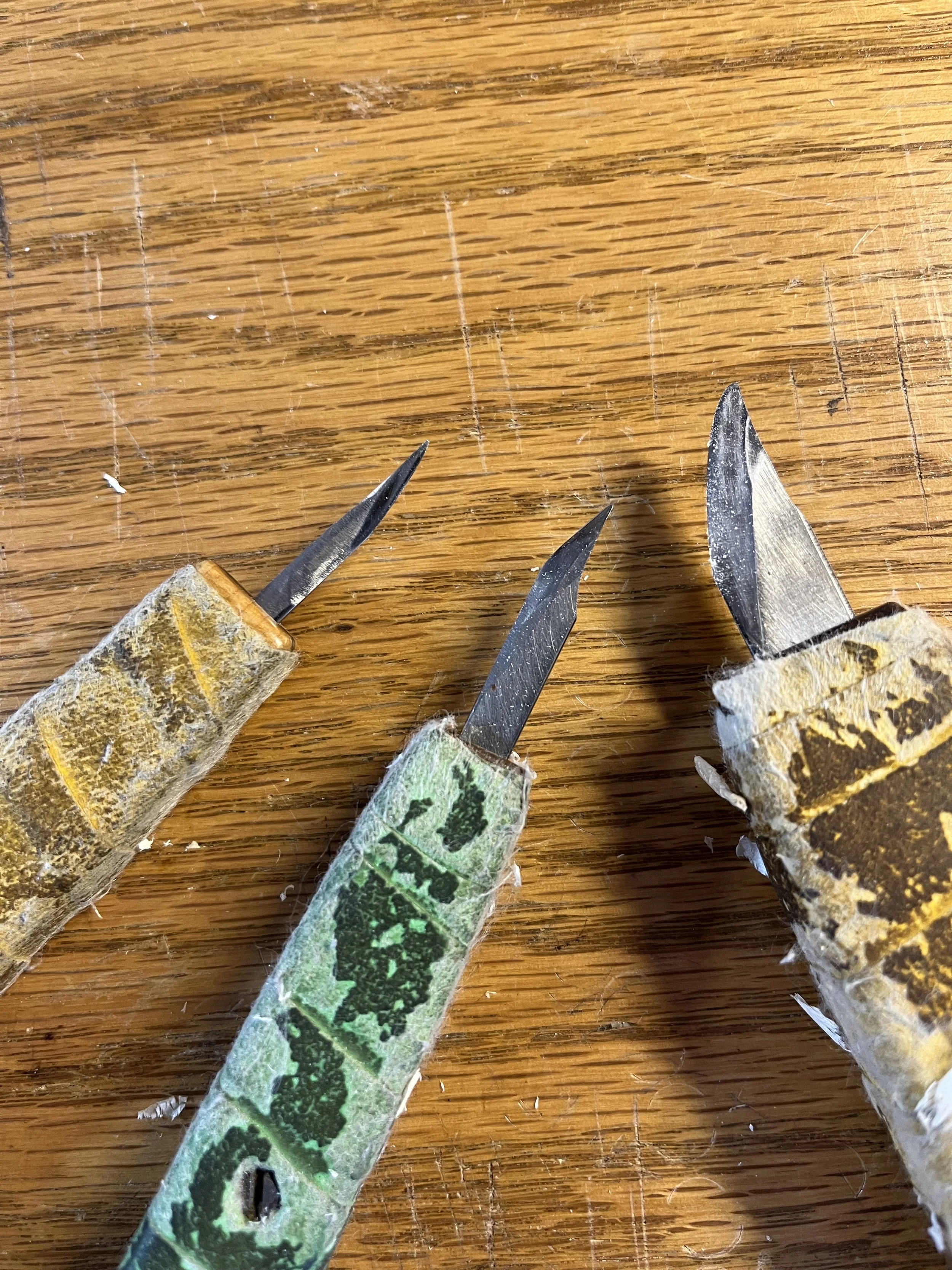 Close-up of three knives with worn handles laying on a wooden surface.