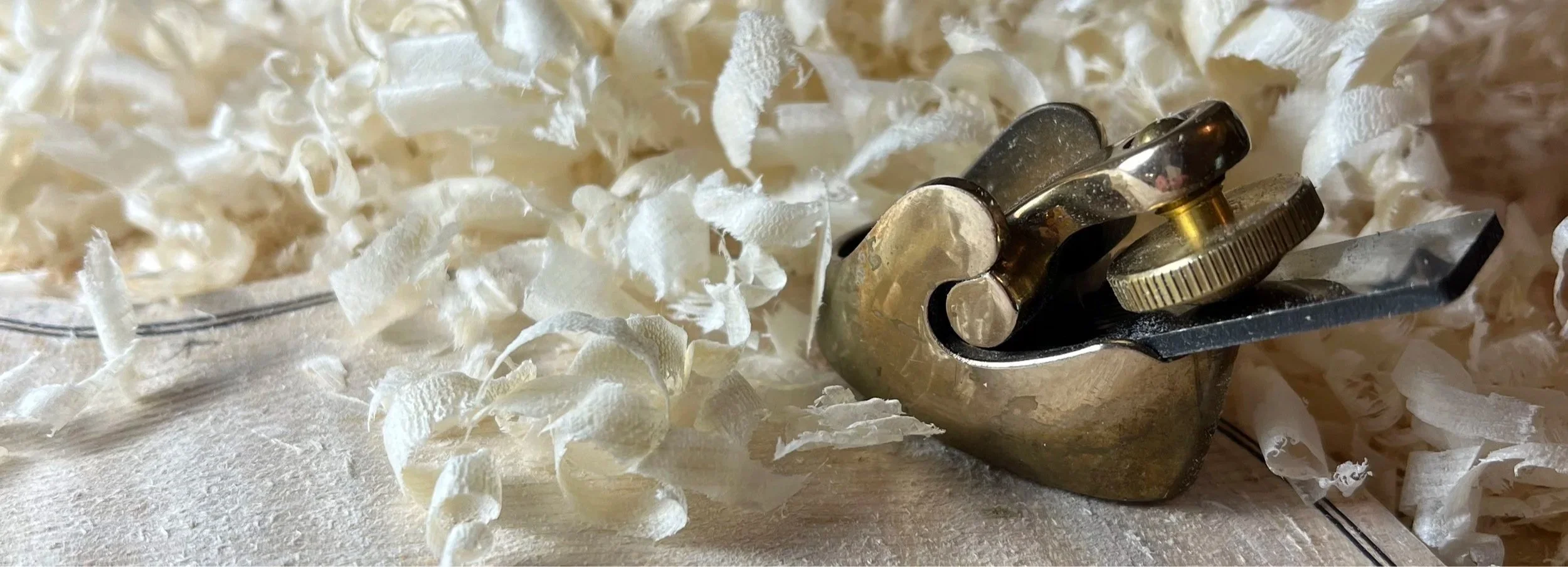 Close-up of a woodworking chisel with a brass adjustment knob resting on a surface surrounded by wood shavings.