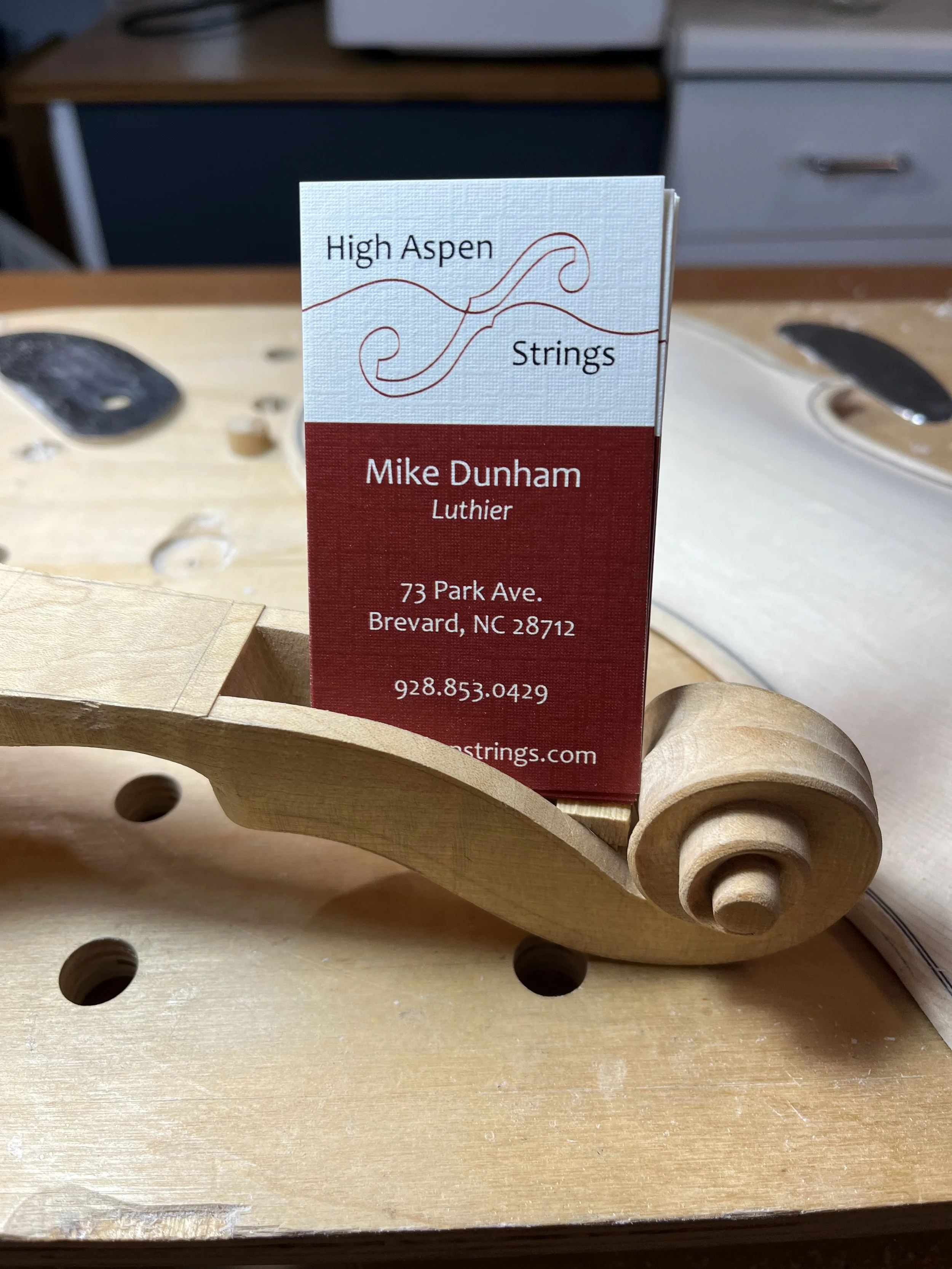 A business card placed on a wooden scroll-shaped object, with a workbench in the background.