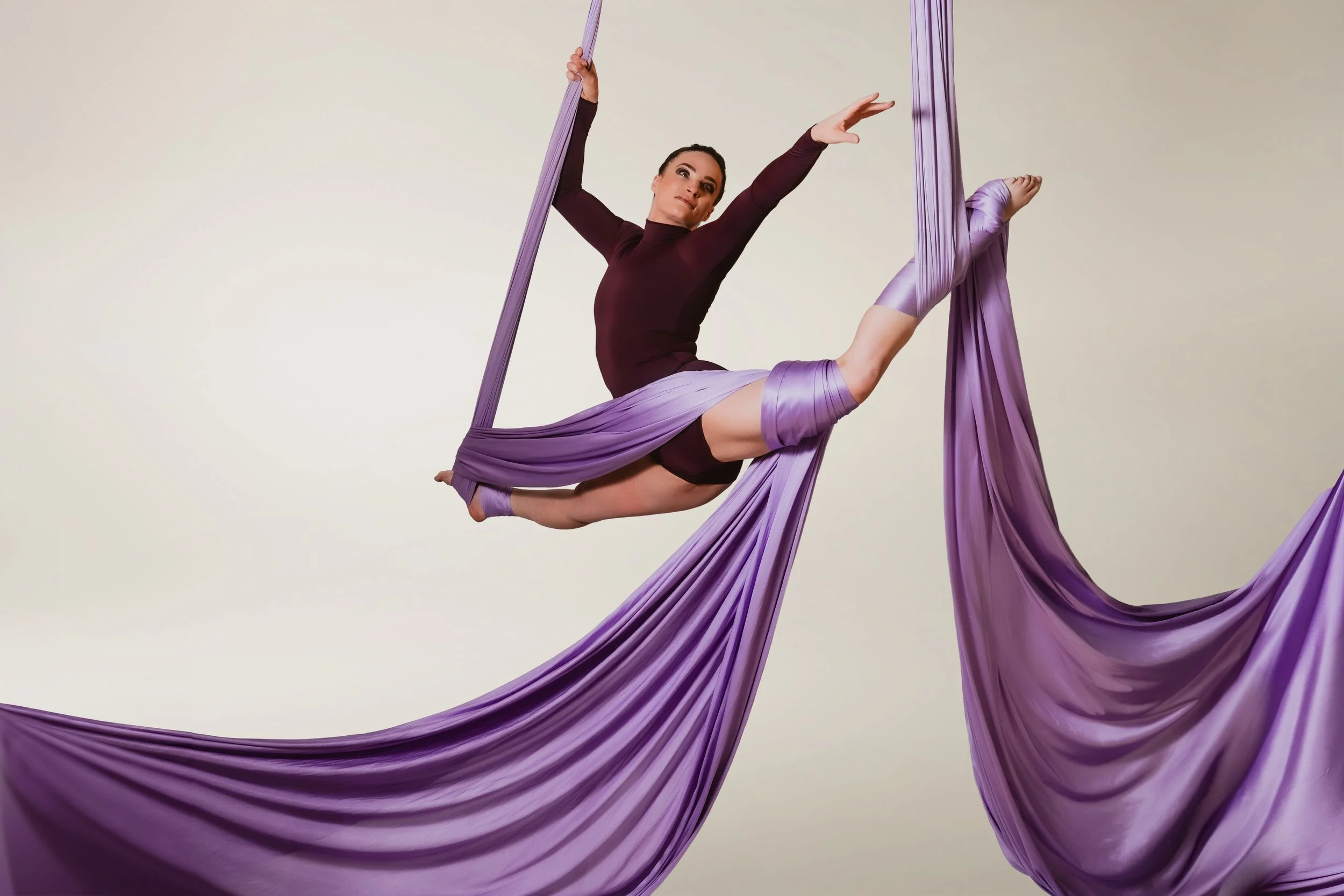 Young woman climbing a white aerial silk