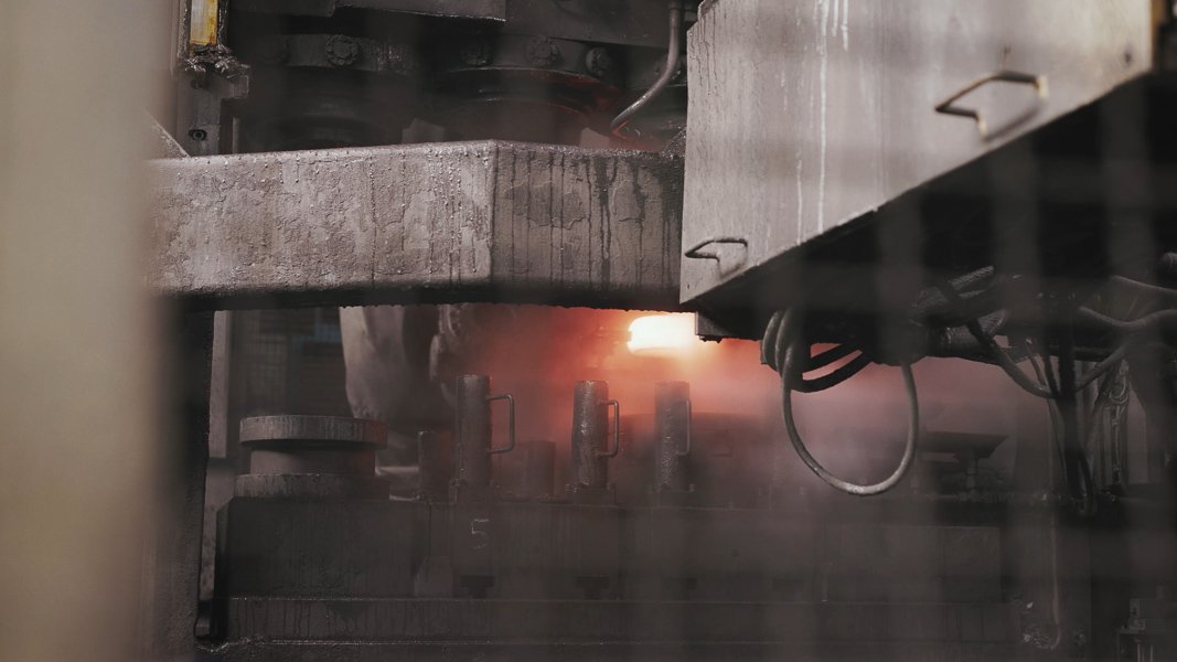 Industrielle Metallbearbeitungsmaschine mit glühendem Metallstück, umgeben von Dampf und mechanischen Komponenten.