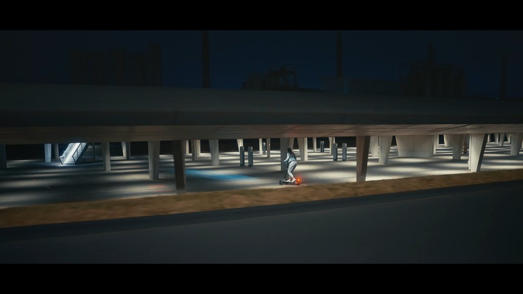 Person auf E-Scooter in beleuchtetem, modernen architektonischen Raum bei Nacht.