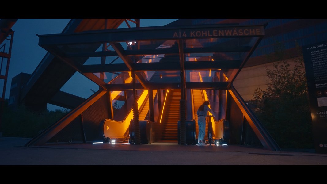 Eine beleuchtete Rolltreppe in der Nacht, die in die Kohlenwäsche führt, mit einer Person, die am unteren Ende steht.